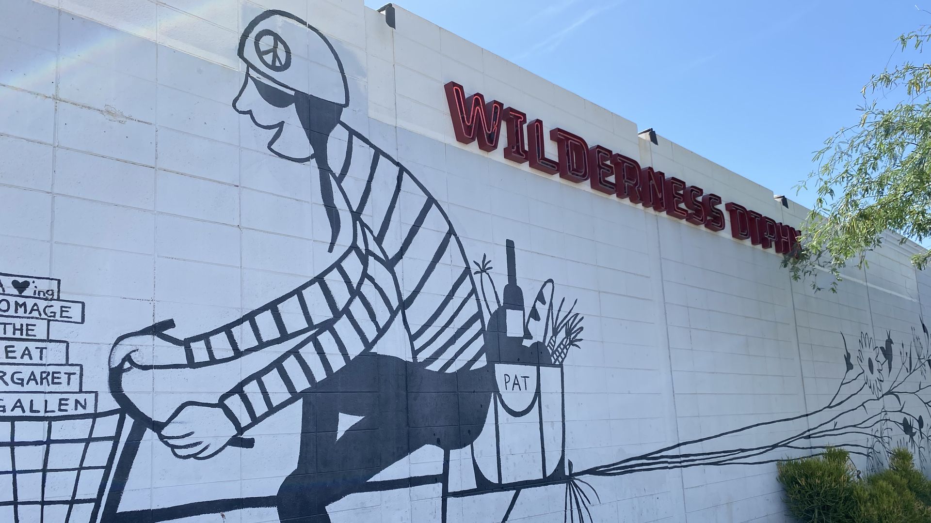 The side a building painted white with a mural of a man on a bicycle and a sign that says Wilderness.