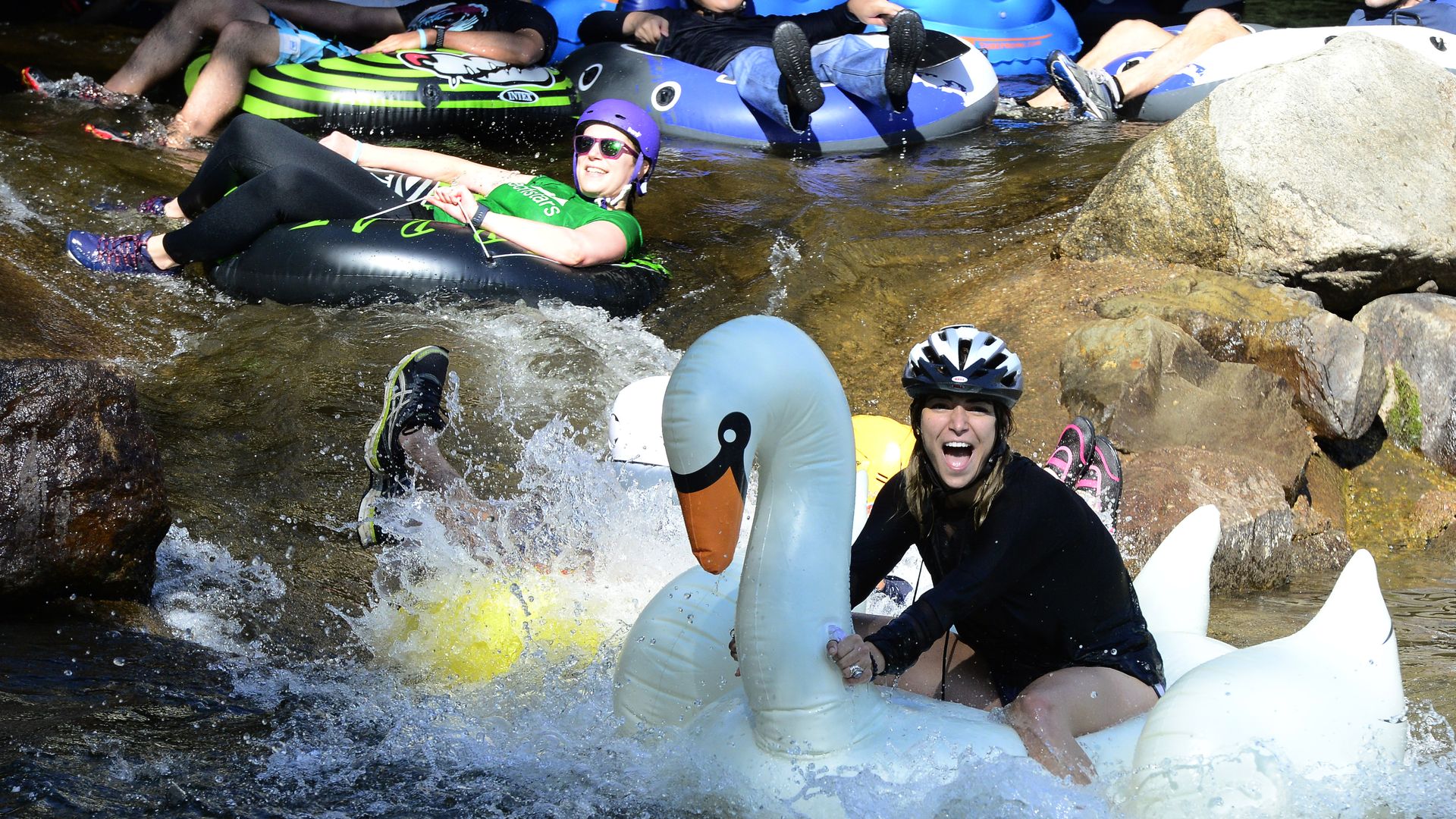 A woman rides a large swan tube down a rapid on Boulder Creek as other tubers are seen in the background