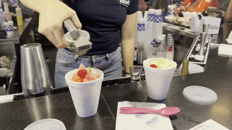 Image shows a person squeezing fresh lime juice over two frozen drinks at a bar.