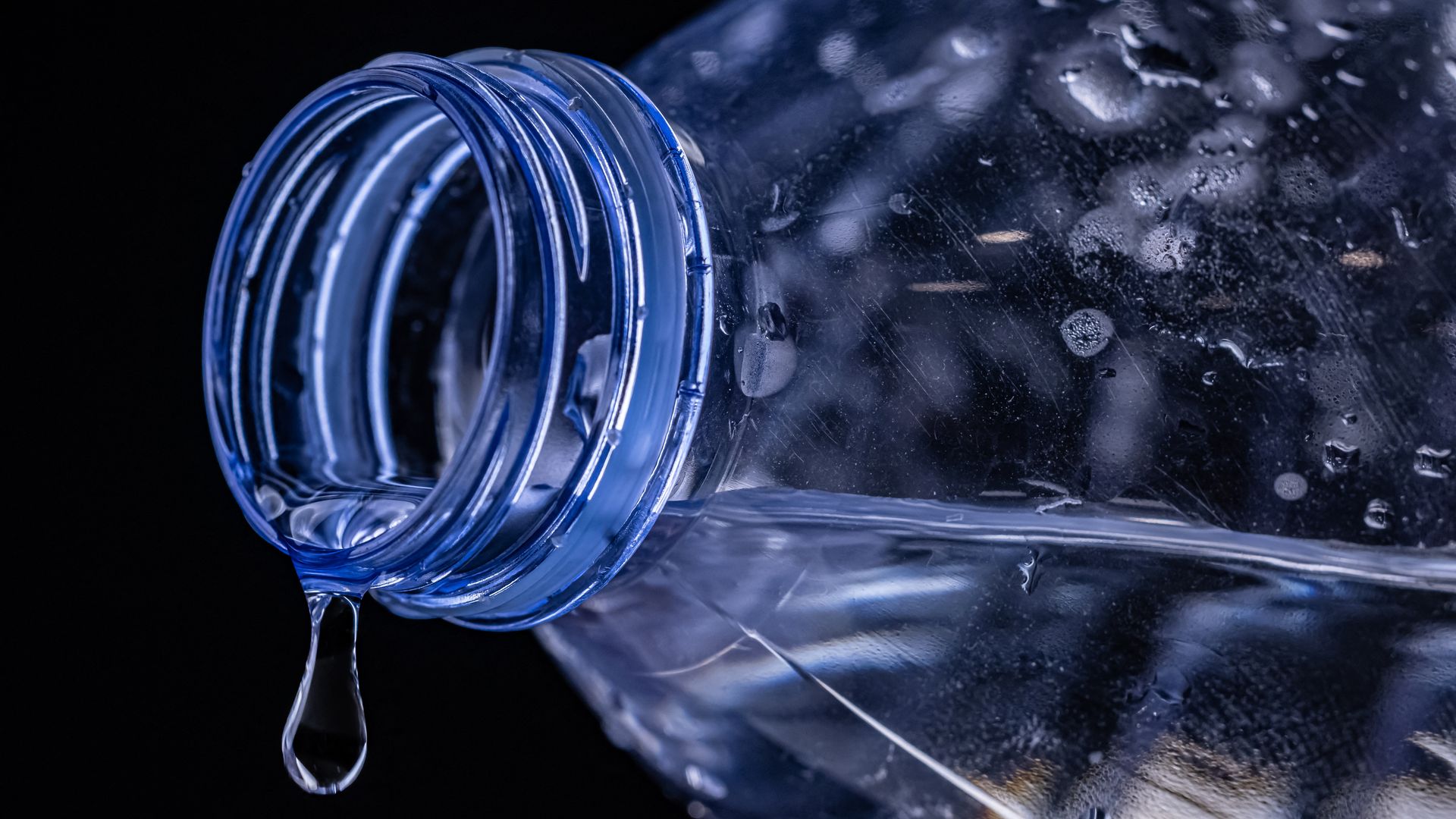 A plastic bottle with a drop of water falling from its lip.