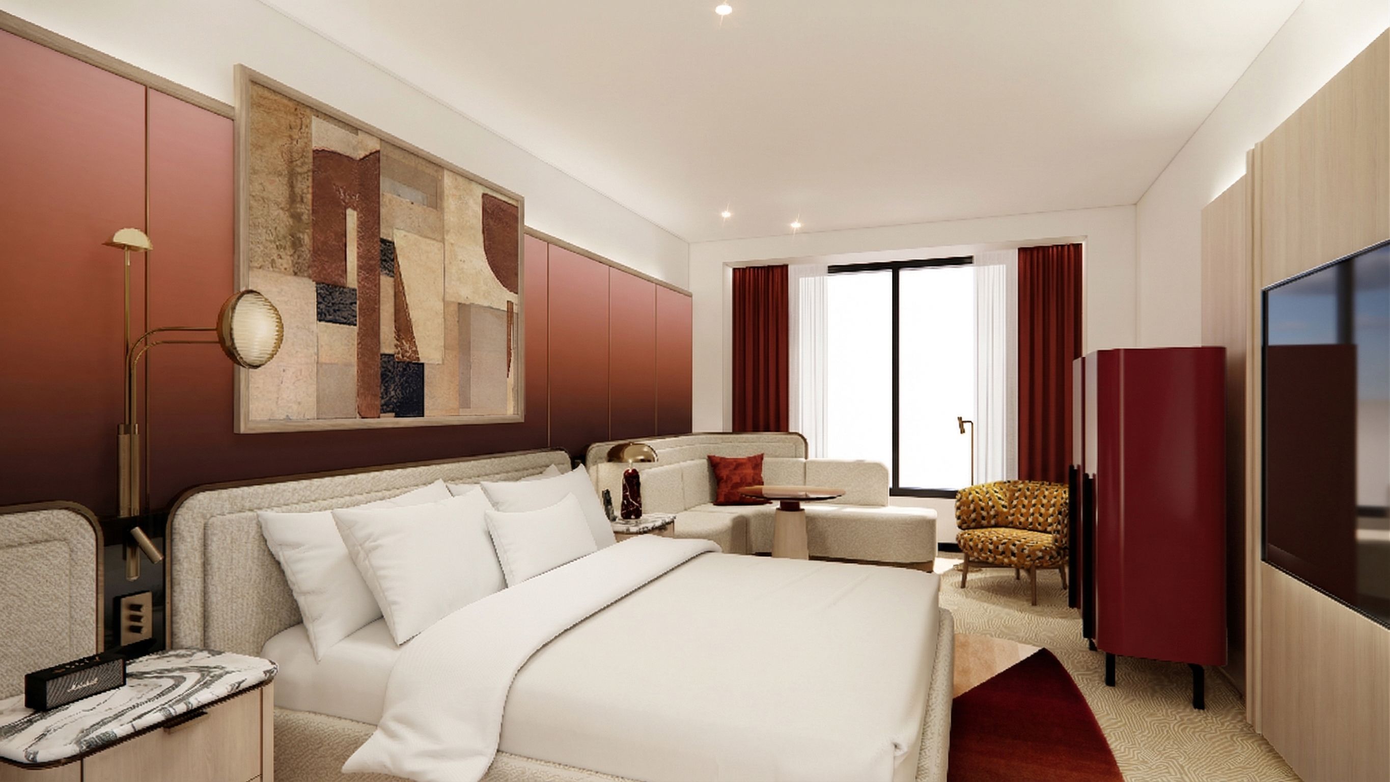 Hotel suite with a large white bed in the foreground, beige headboard, burgundy walls, a gold floor lamp, abstract art, a cream sofa, a patterned yellow chair, and a TV by tall windows with red drapes.