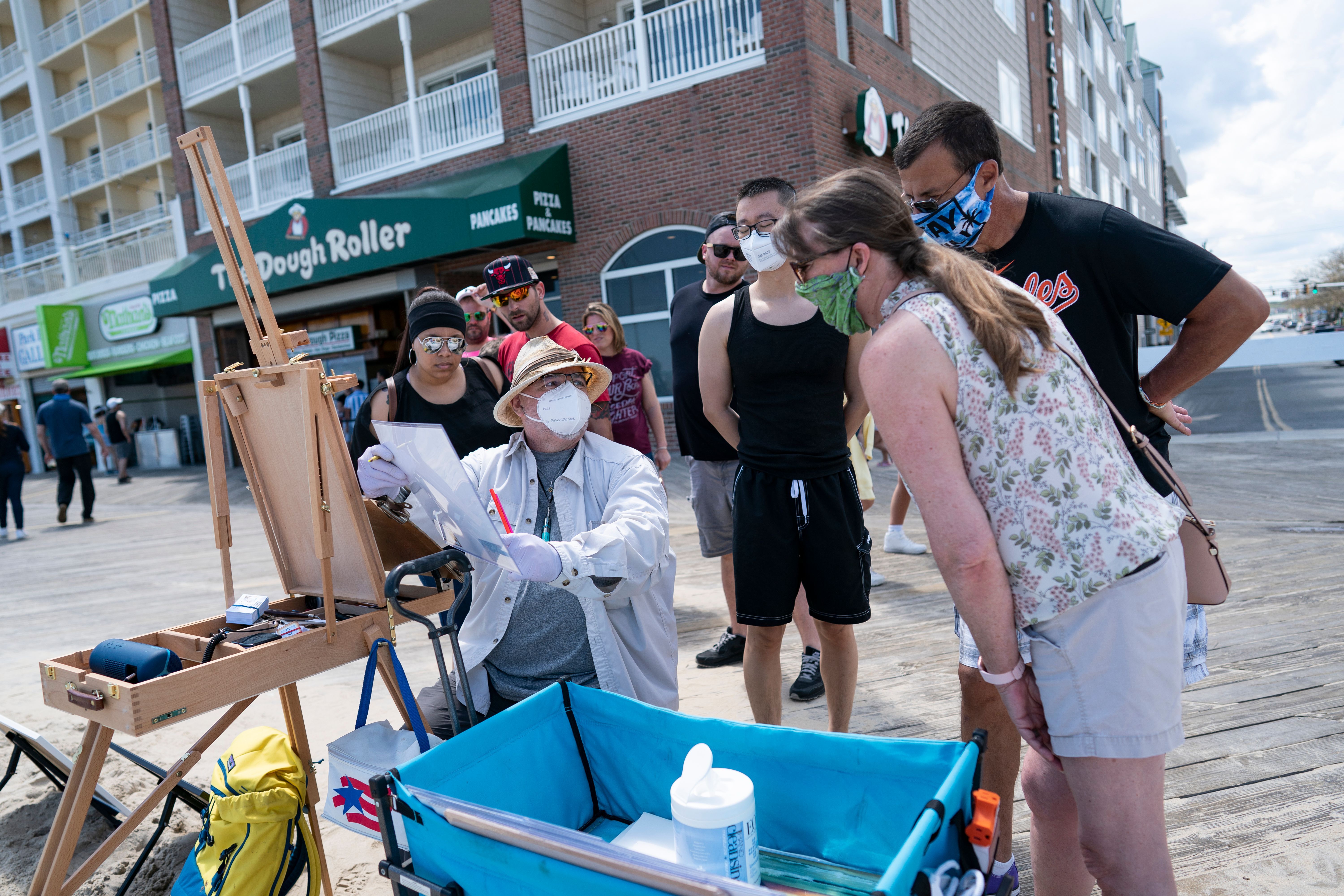 In this image, an artist paints for a small crowd. Most are wearing face masks
