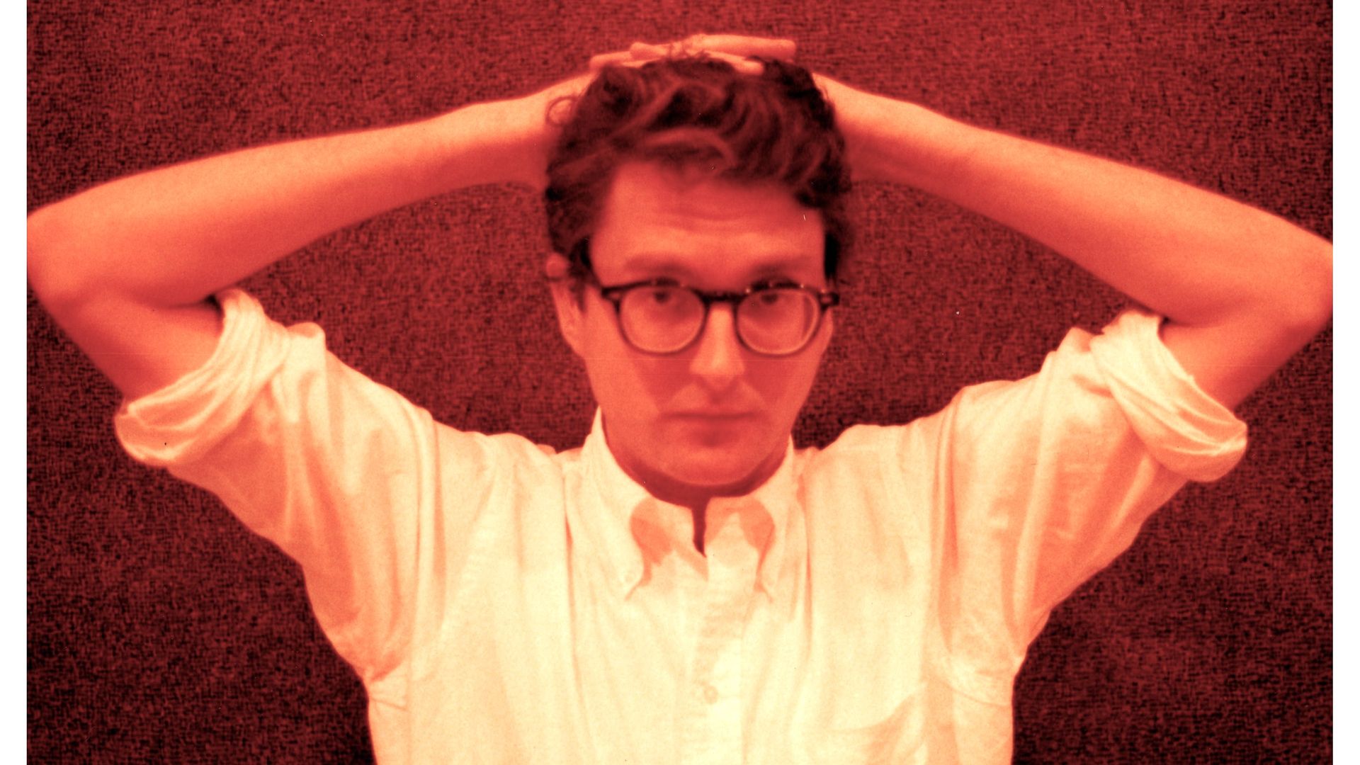 Artist John Wilcox with his hands behind his head, looking directly at the camera.