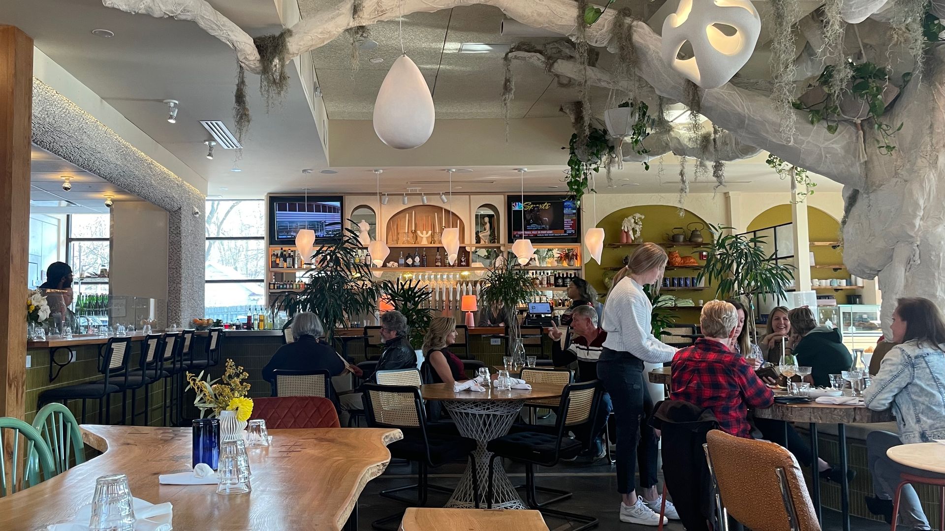 The interior of a restaurant with a tree in the middle and a server at a table of customers