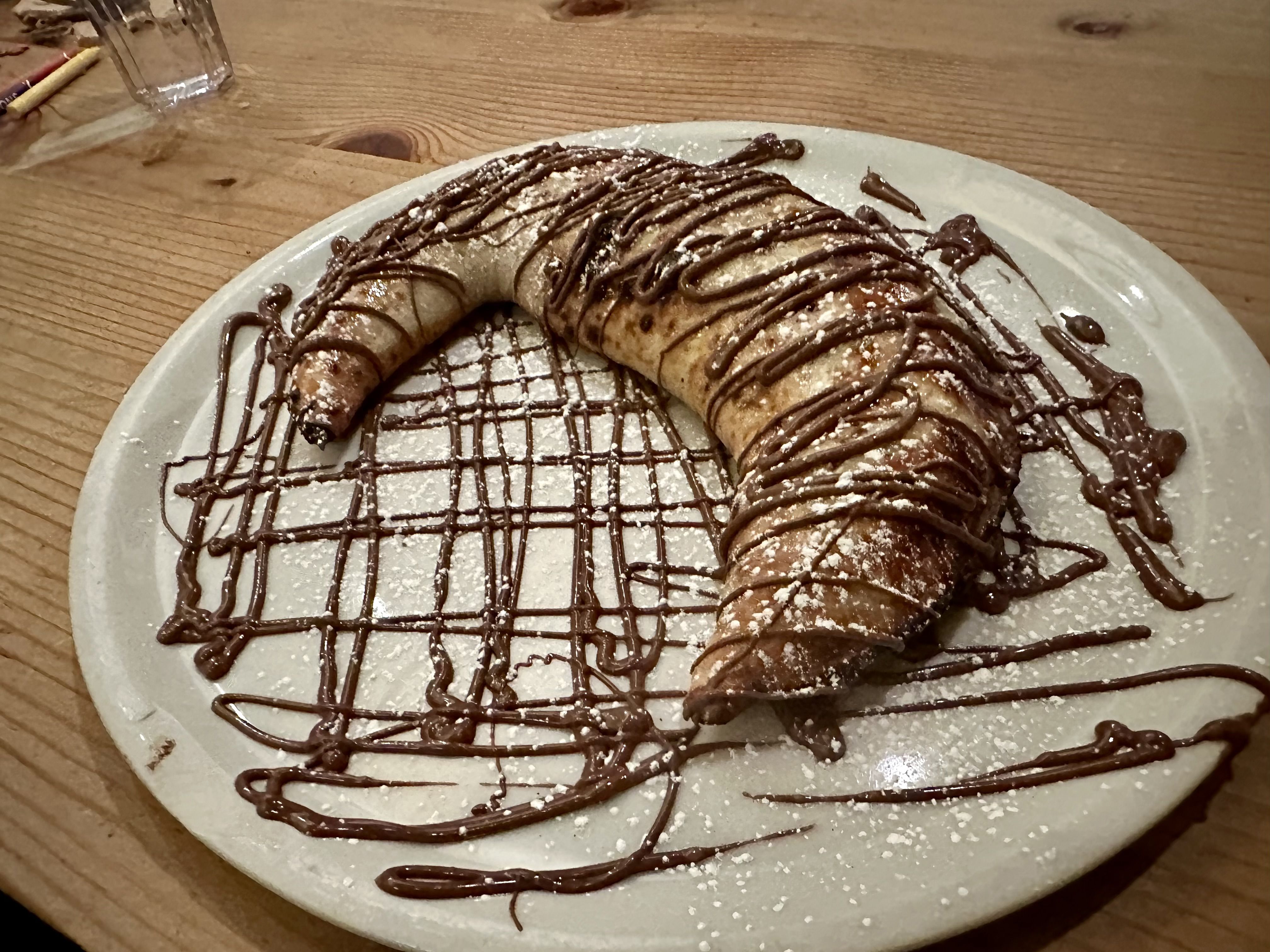 A moon-shaped dough creation with chocolate drizzled over it and some powdered sugar sprinkled on top.