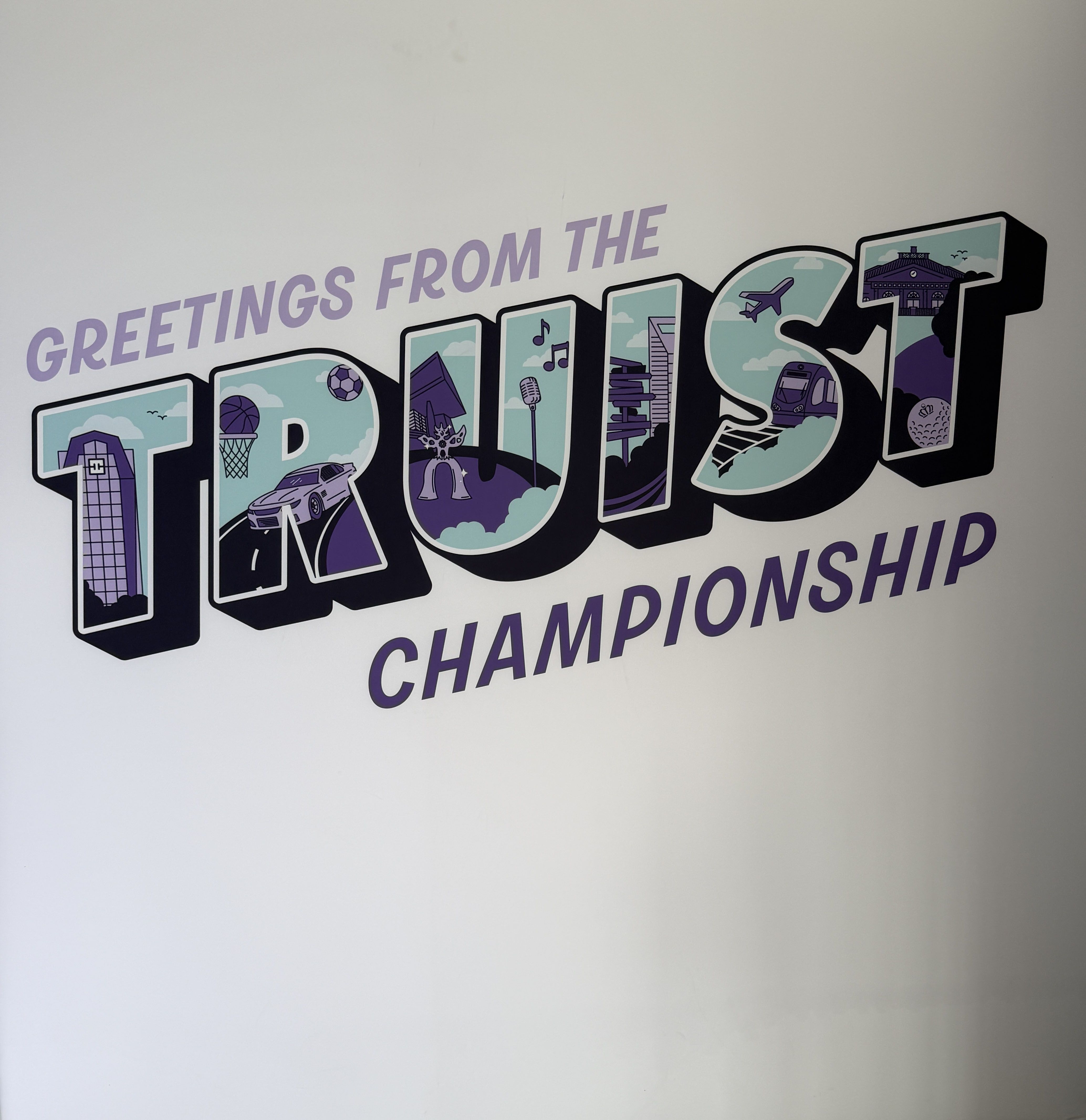 White wall mural featuring lavender 'GREETINGS FROM THE' text above large colored block letters filled with city icons like planes, buildings, and stadiums; the word 'CHAMPIONSHIP' appears below.