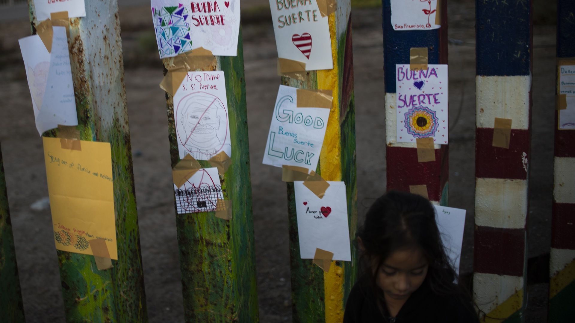 A young girl stands next to messages tacked to the US-Mexico border