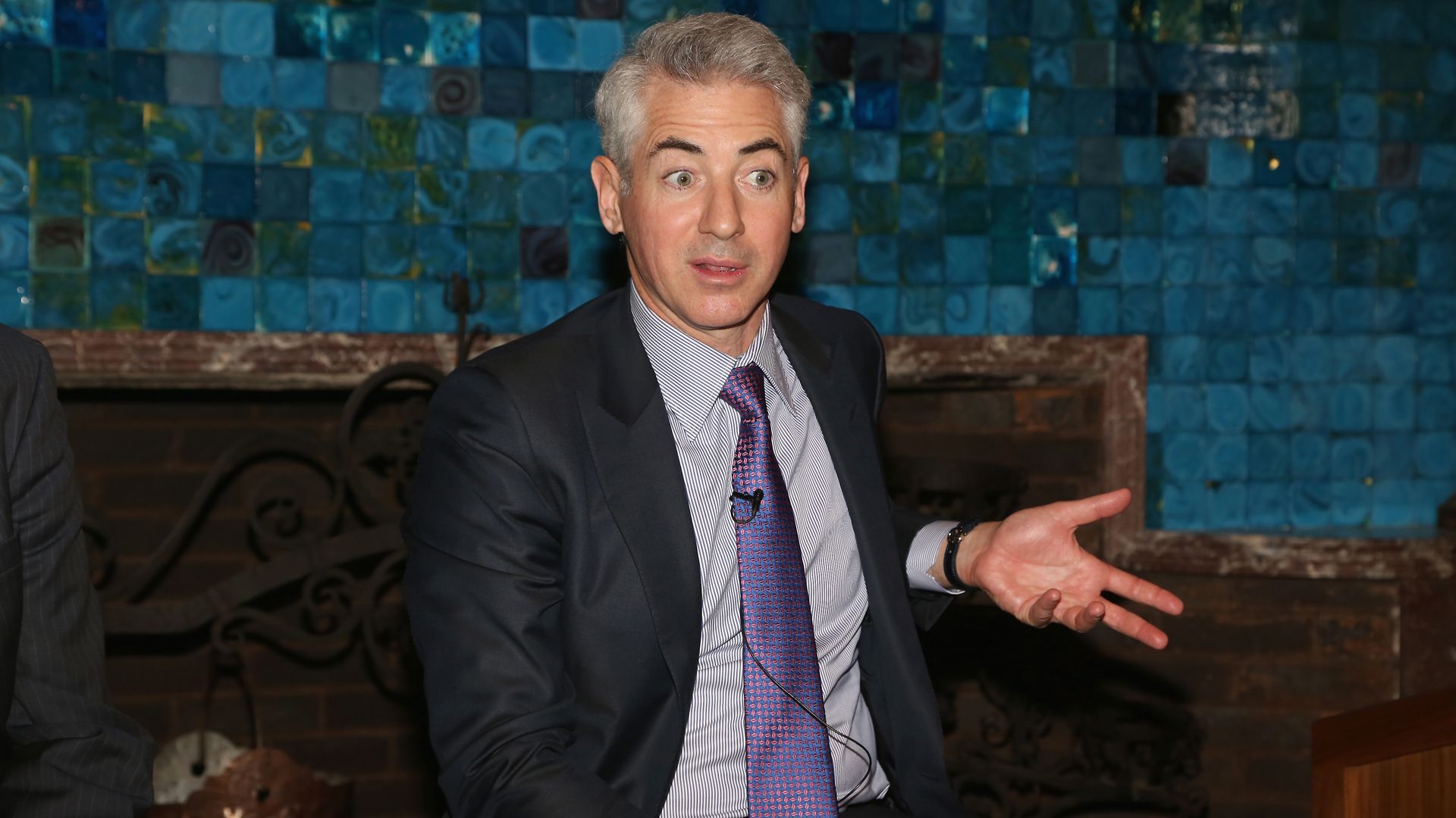 In this image, Ackman sits and talks while gesturing with one hand and wearing a suit and tie.