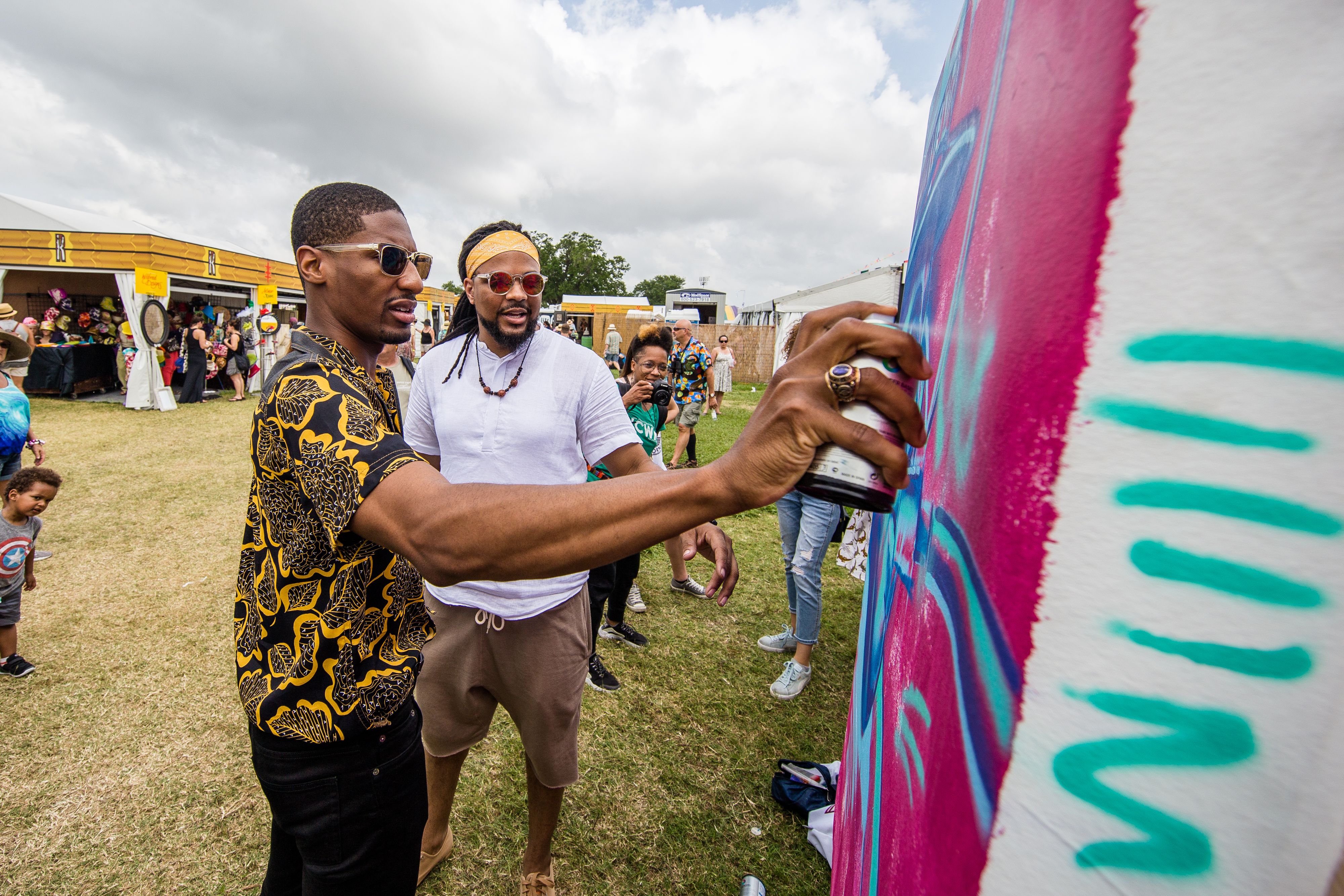 Jon Batiste adds a touch of spray paint to a mural by Brandan "BMike" Odums, who stands to Batiste's left and watches as the musician paints.