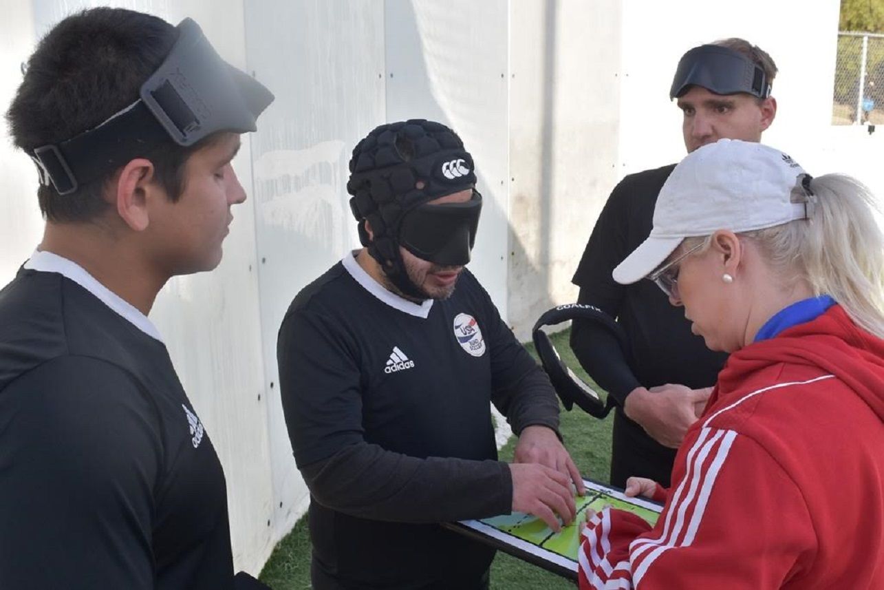 A blind soccer coach and players feel a magnetic strategy board. 