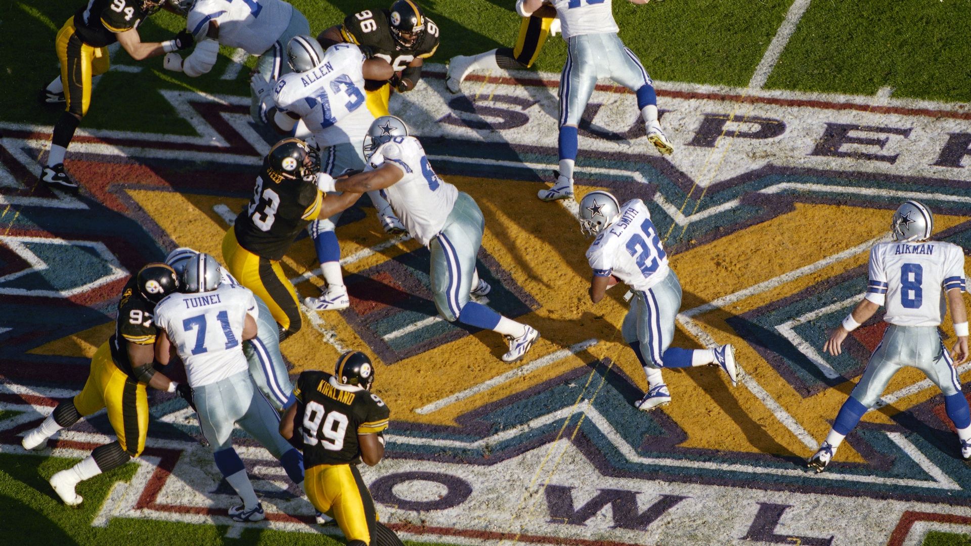 A Dallas Cowboys player is tackled by a Pittsburgh Steelers player while other Cowboys players try to help him