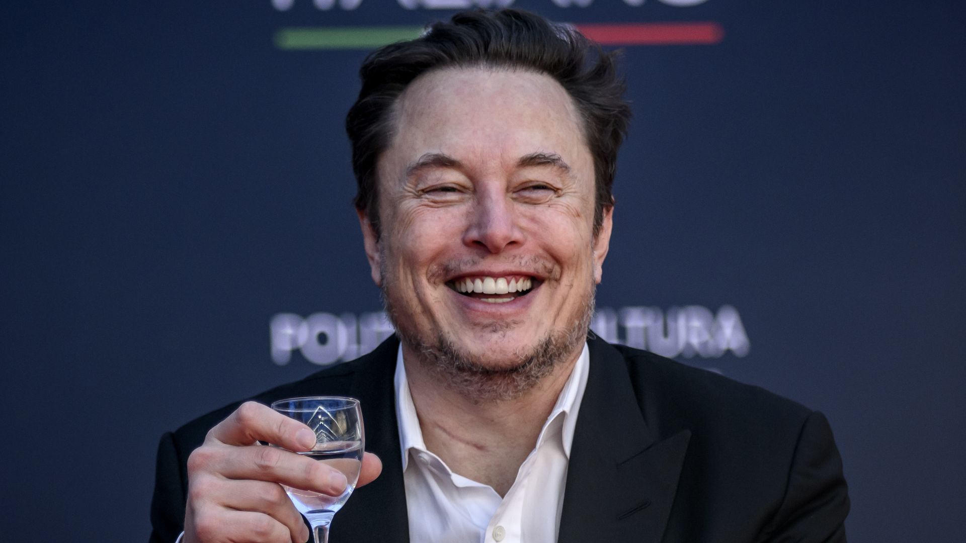 Elon Musk holding a glass and smiling.