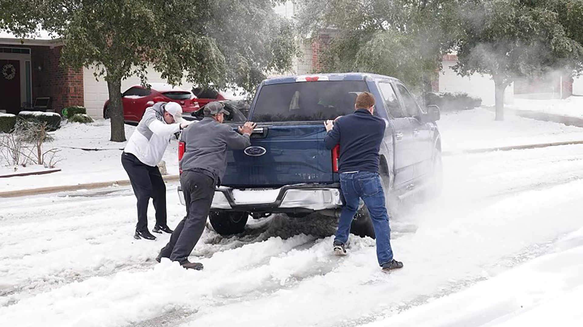 Residents help a pickup driver get out of ice on the road in Round Rock, Texas, on February 17, 2021, after a winter storm