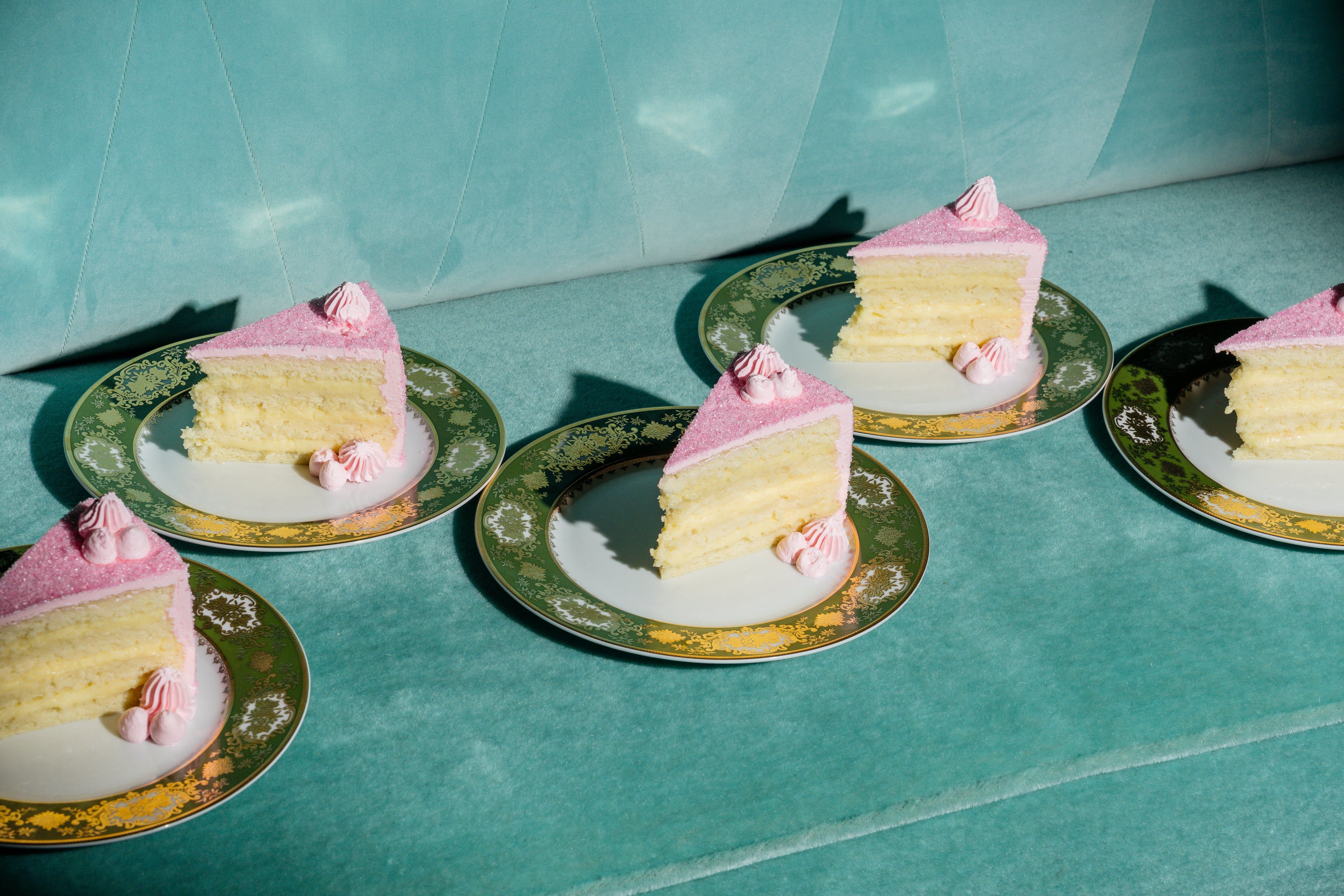 Pieces of Champagne cake with pink and white frosting on a green background
