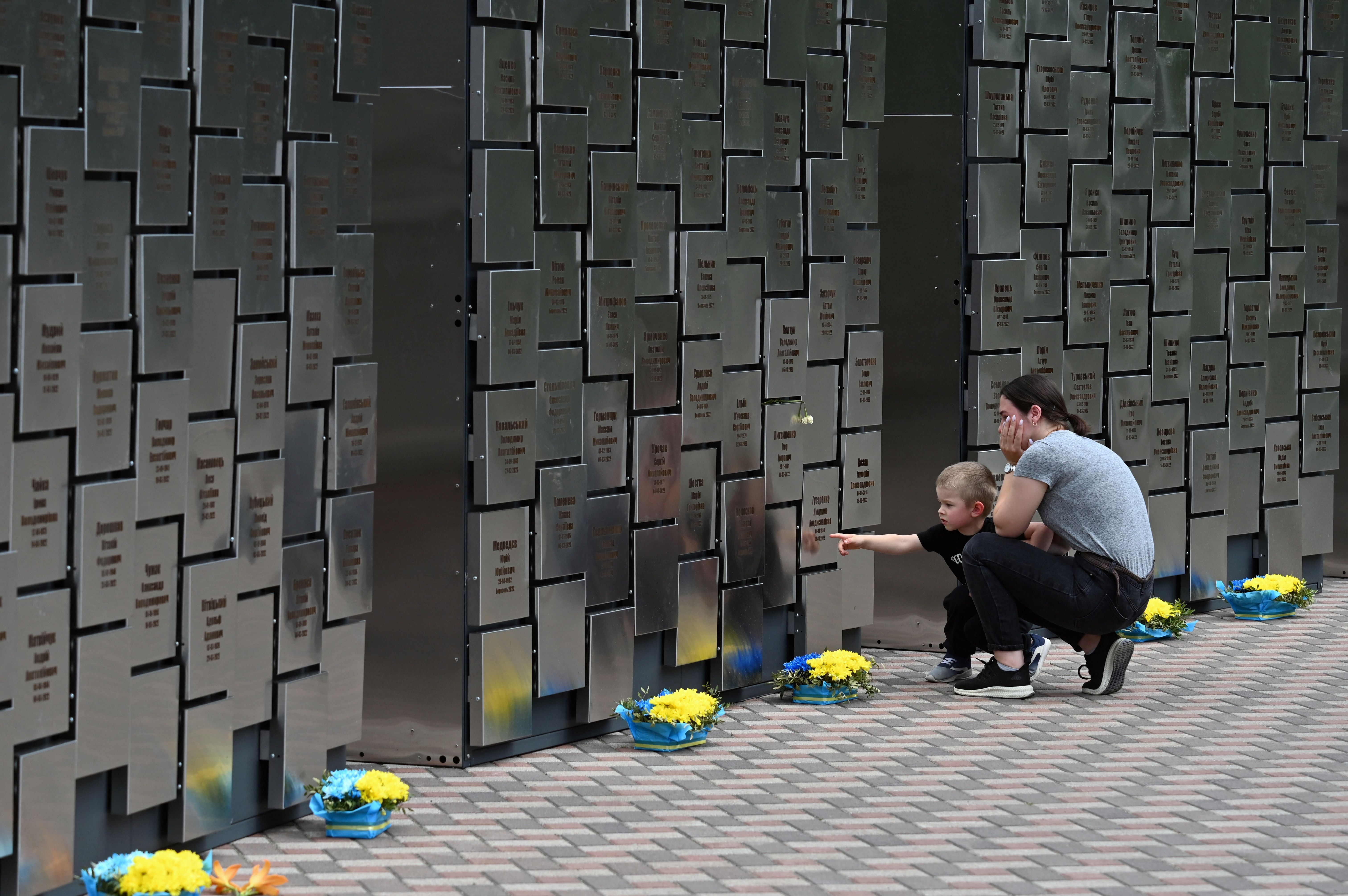  A young woman reacts as she stands with her son in front of a recently inaugurated memorial including 501 plates bearing the names of identified local civilians killed by Russian troops during their occupation of Bucha, north of Kyiv, on July 3, 2023. 