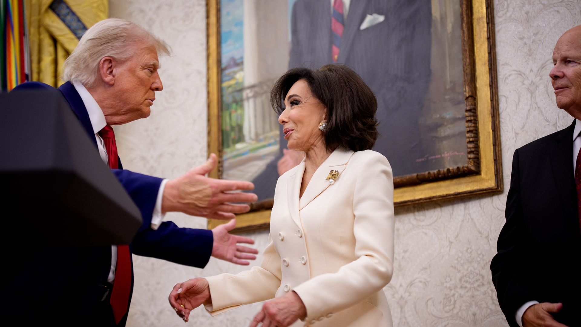 Trump reaches out toward Jeanine Pirro, in a white suit, inside the Oval Office.