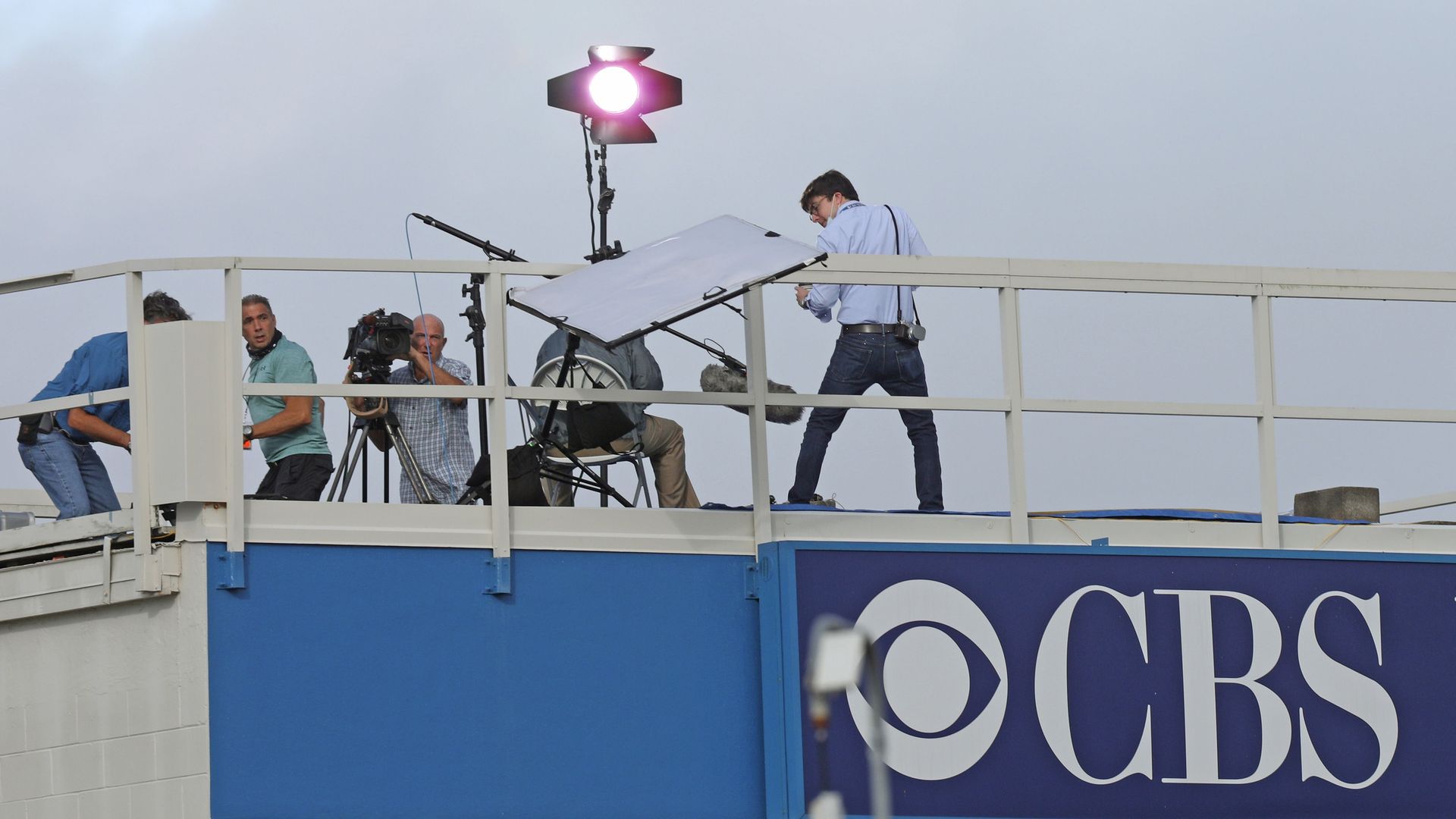 A CBS News crew looks on as a reflector topples over from the wind while preparing to broadcast at the Kennedy Space Center in Florida.