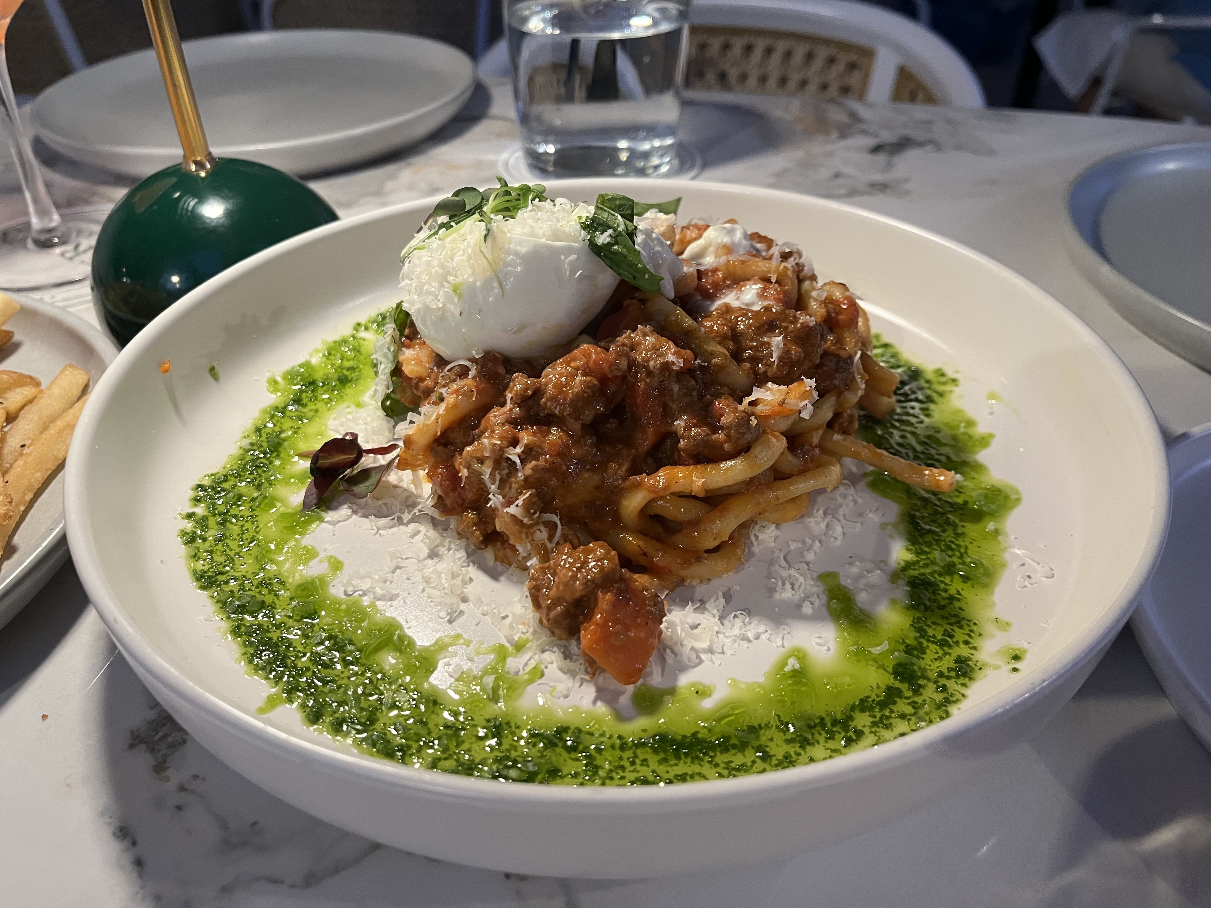 A green ring of pesto surrounds a pile of pasta topped with a white lump of cheese. 