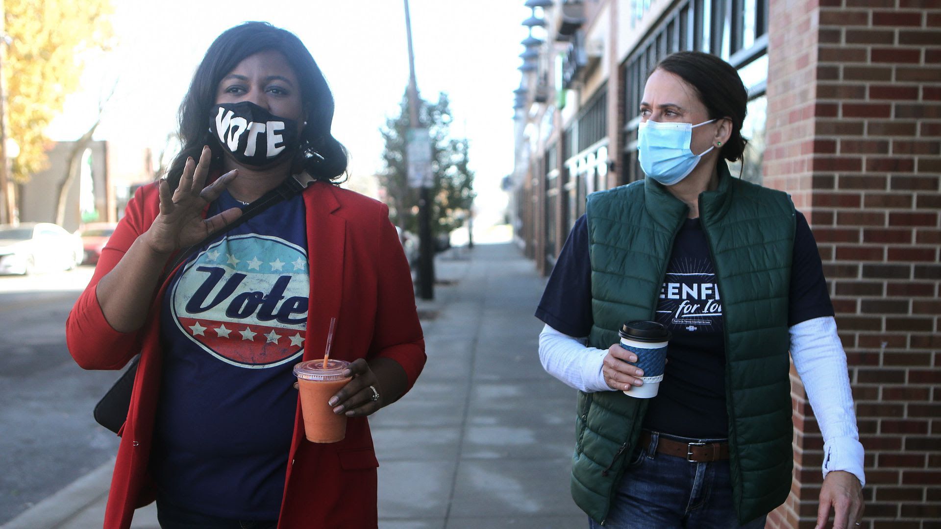 Deidre Dejear, wearing a mask and shirt that say "vote," speaks with former Senate candidate Theresa Greenfield.