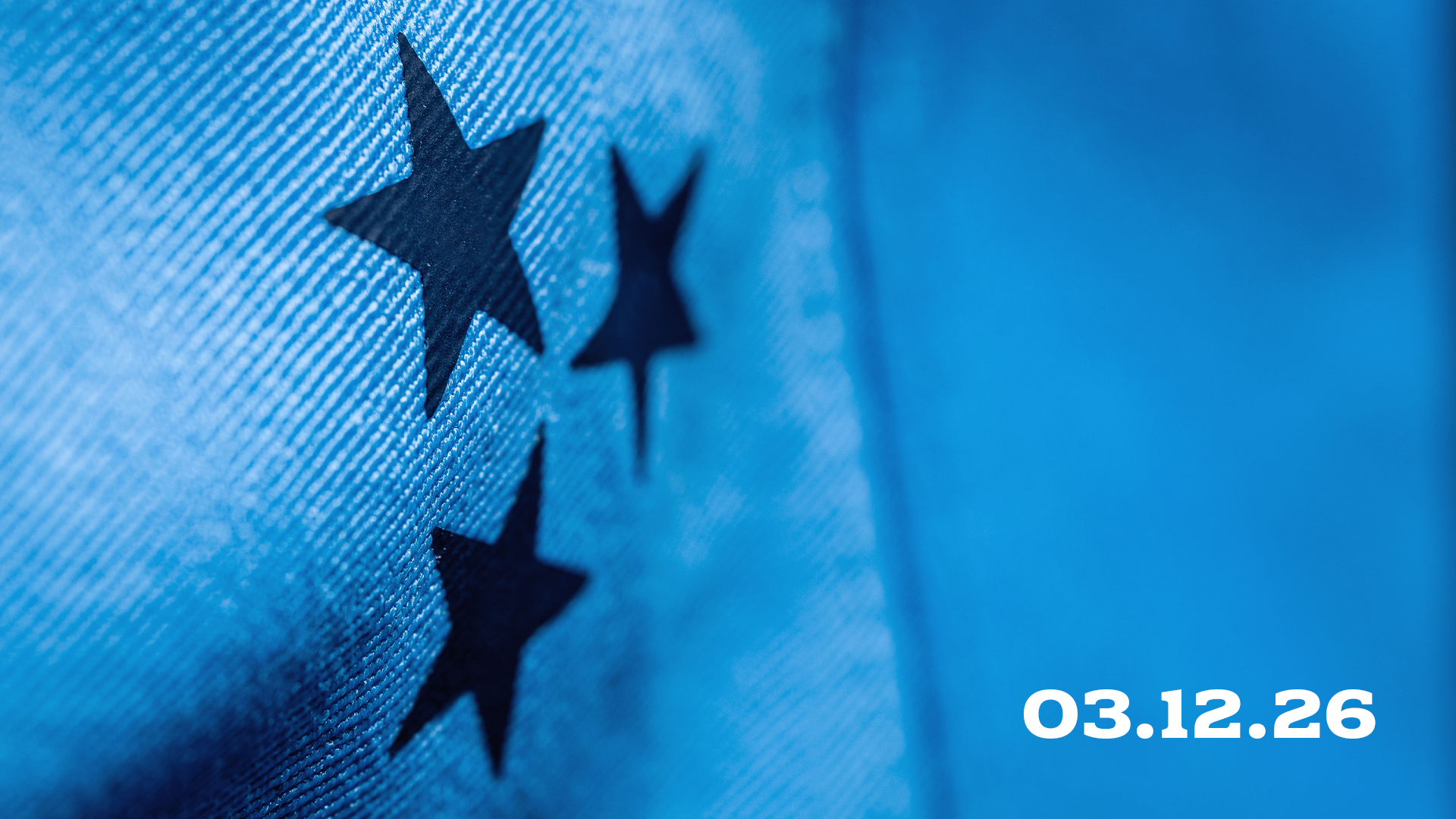 Close-up of a blue fabric with three black stars printed on it, alongside white text displaying the date 03.12.26 on the right side against a blue background.