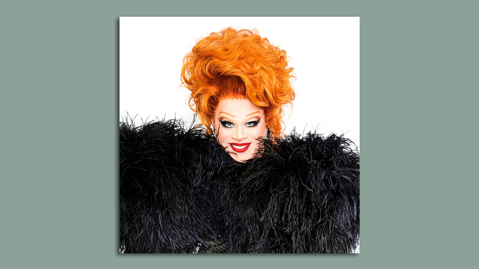 A photo of Nina West with orange hair and black feathers from the top of a dress surrounding her face