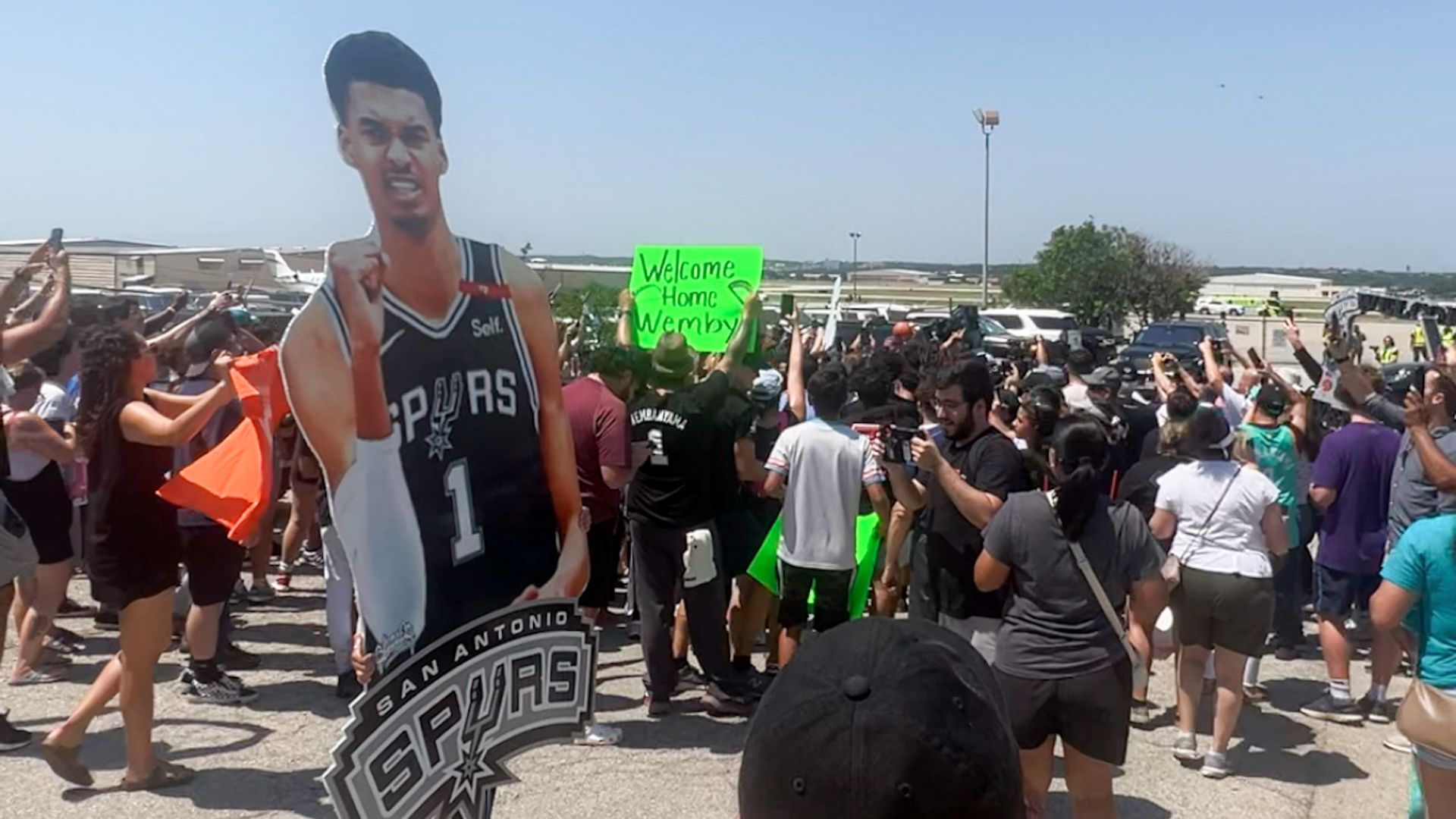 A crowd of people holding posters gather to meet Victor Wembanyama at the airport.