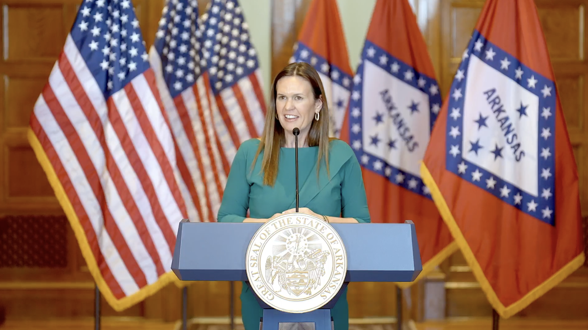 A photo of Gov. Sarah Huckabee Sanders flanked by American and Arkansas flags. 