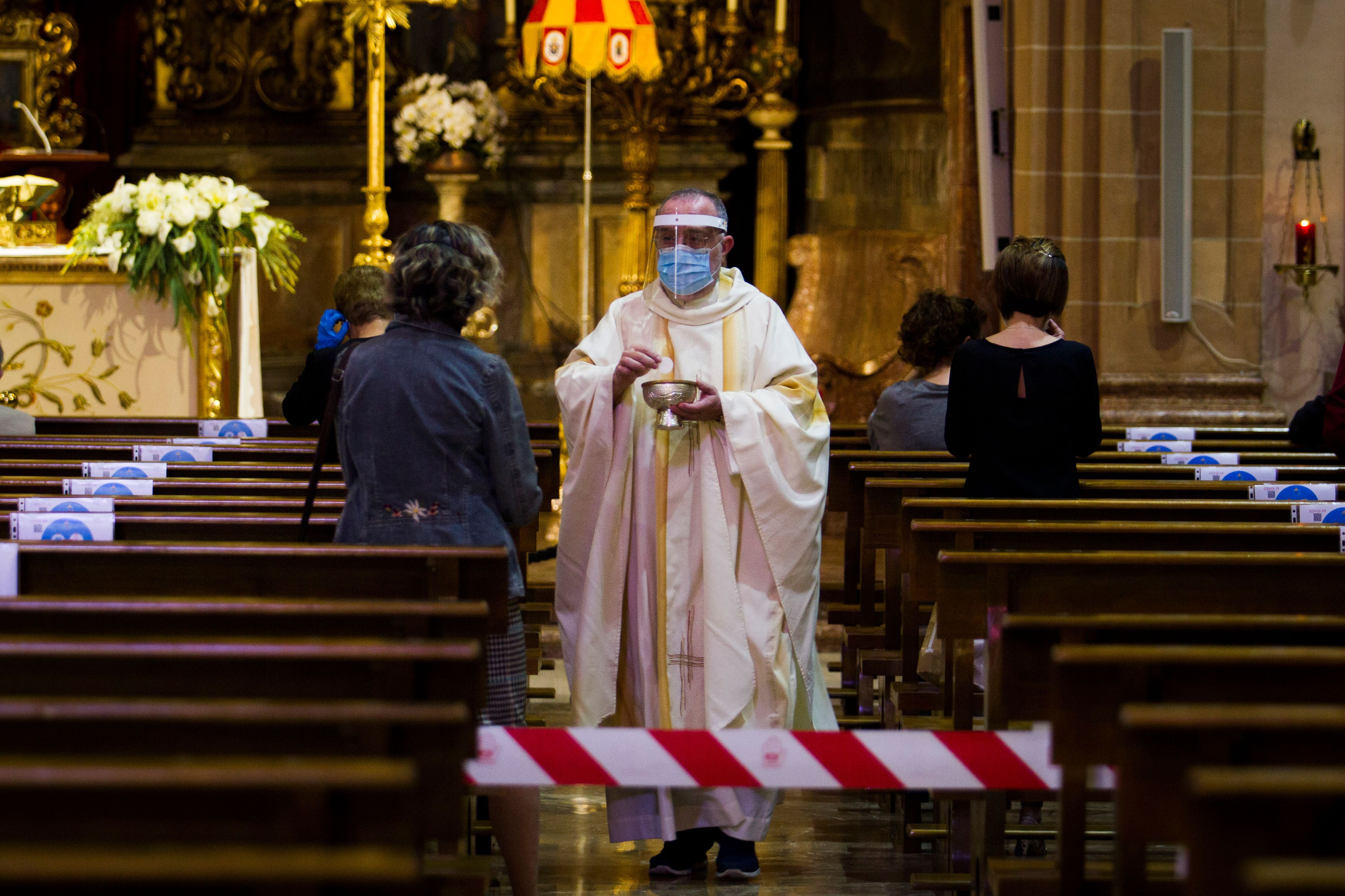 In this image, a priest wearing protective gear anoints the head of a church-goer