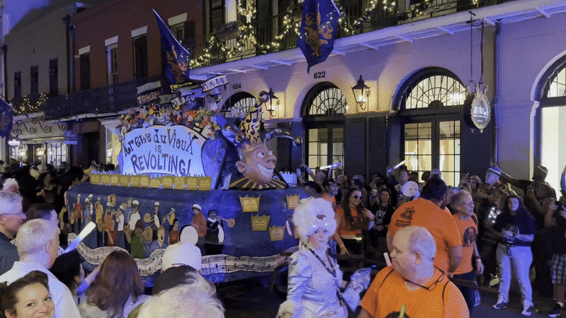 A title float is pulled down a French Quarter street. The float says "Krewe du Vieux is revolting!"
