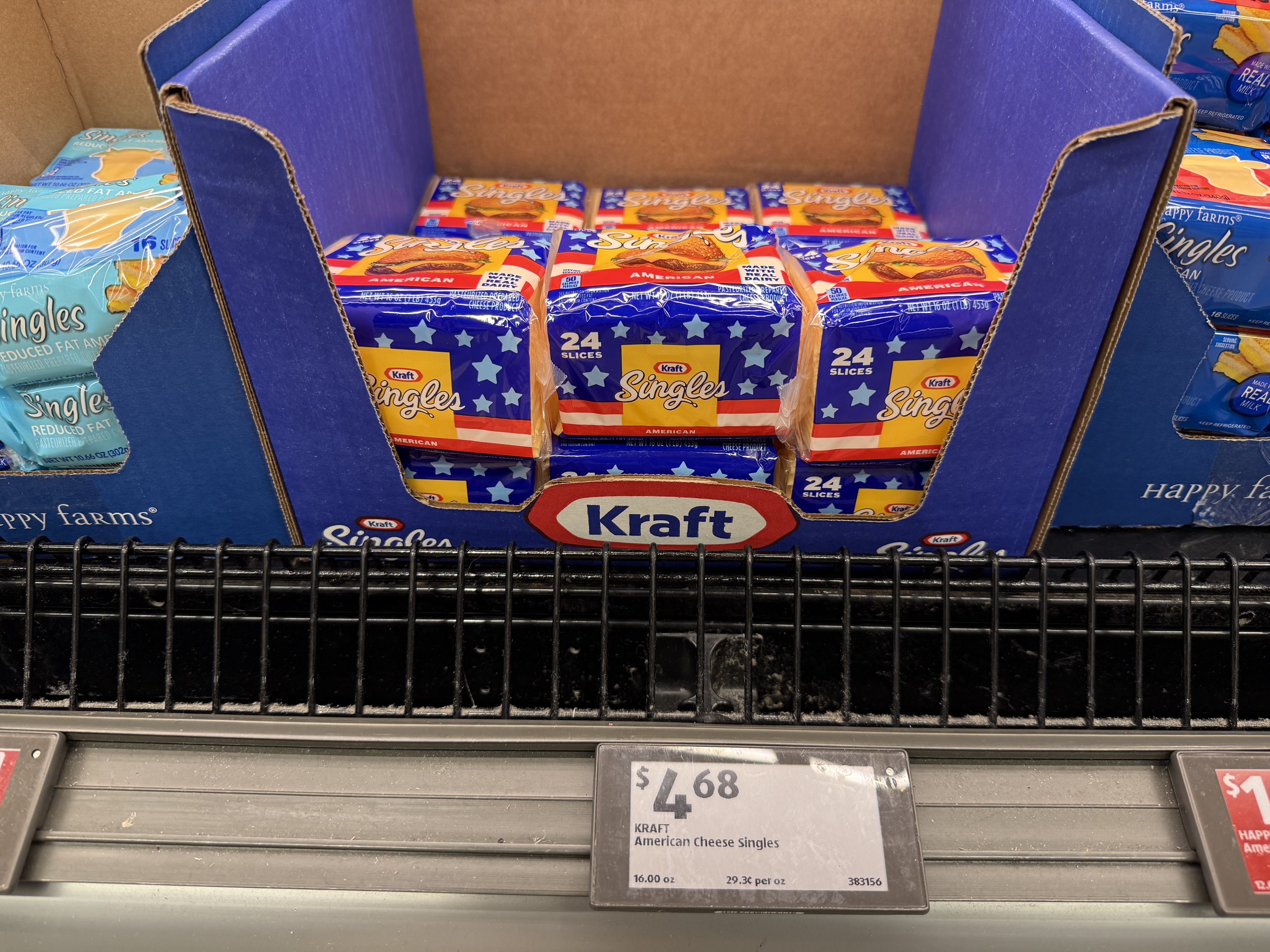 Blue display box holds Kraft American Cheese Singles packs in red, white, and blue with star designs; price tag shows $4.68 on a shelf.