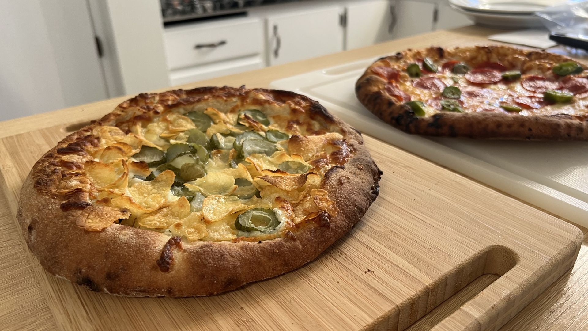 Two frozen pizzas: one with pickles and potato chips, the other with jalapeños and pepperoni