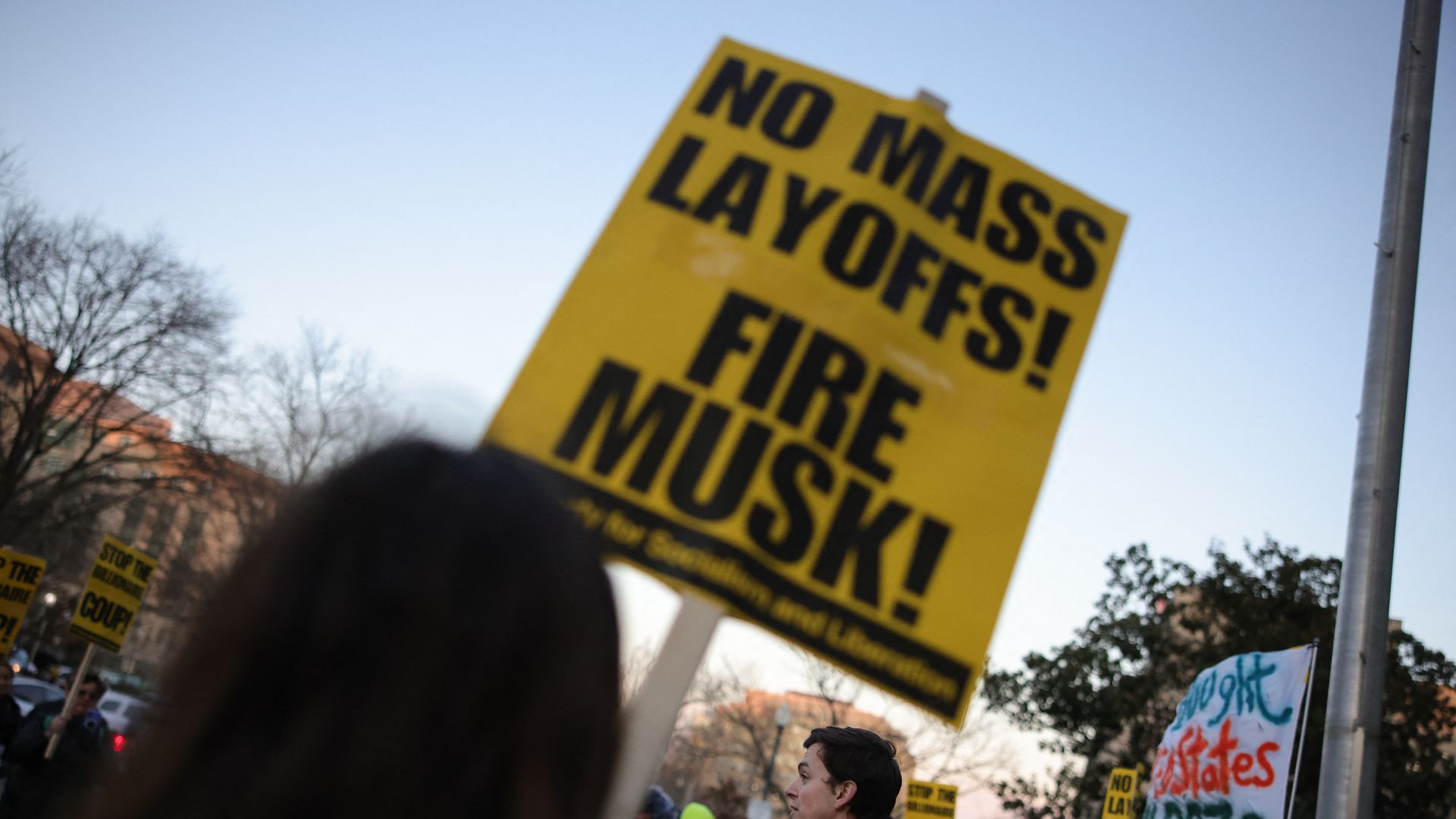 A sign reads "no mass layoffs! Fire Musk!"