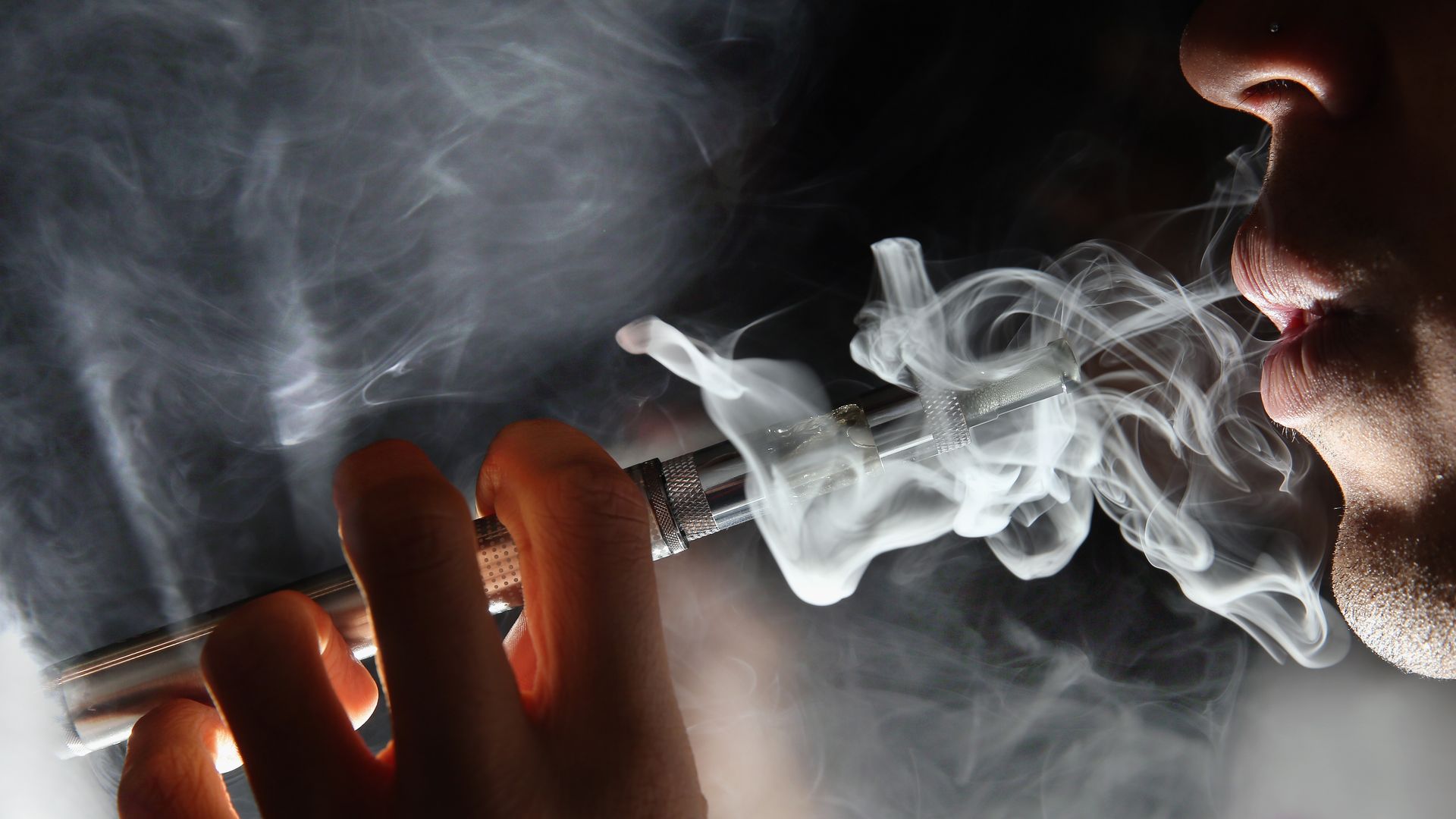 In this image, a man smokes with a vape