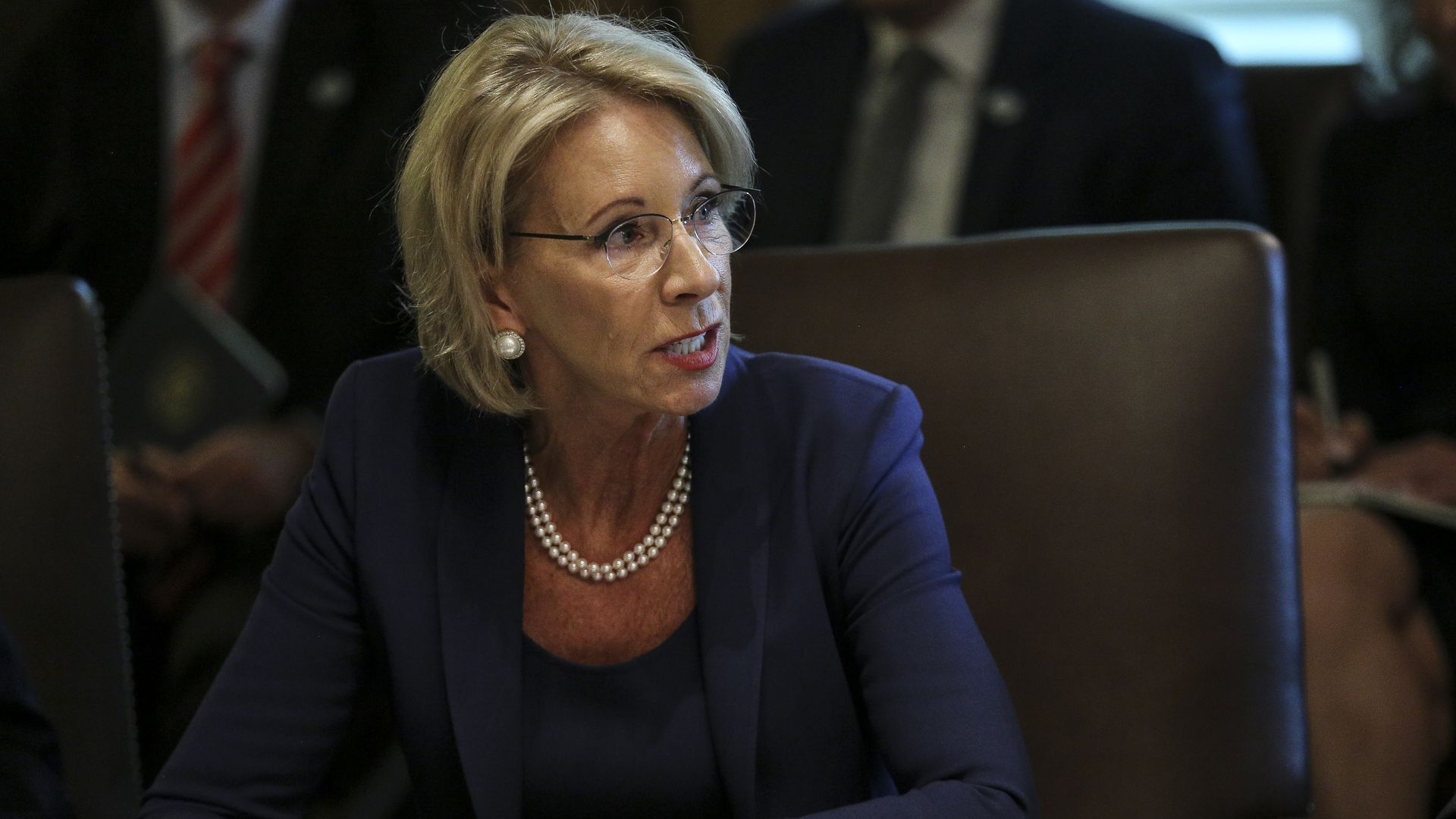 Betsy DeVos sitting in a chair at a meeting.