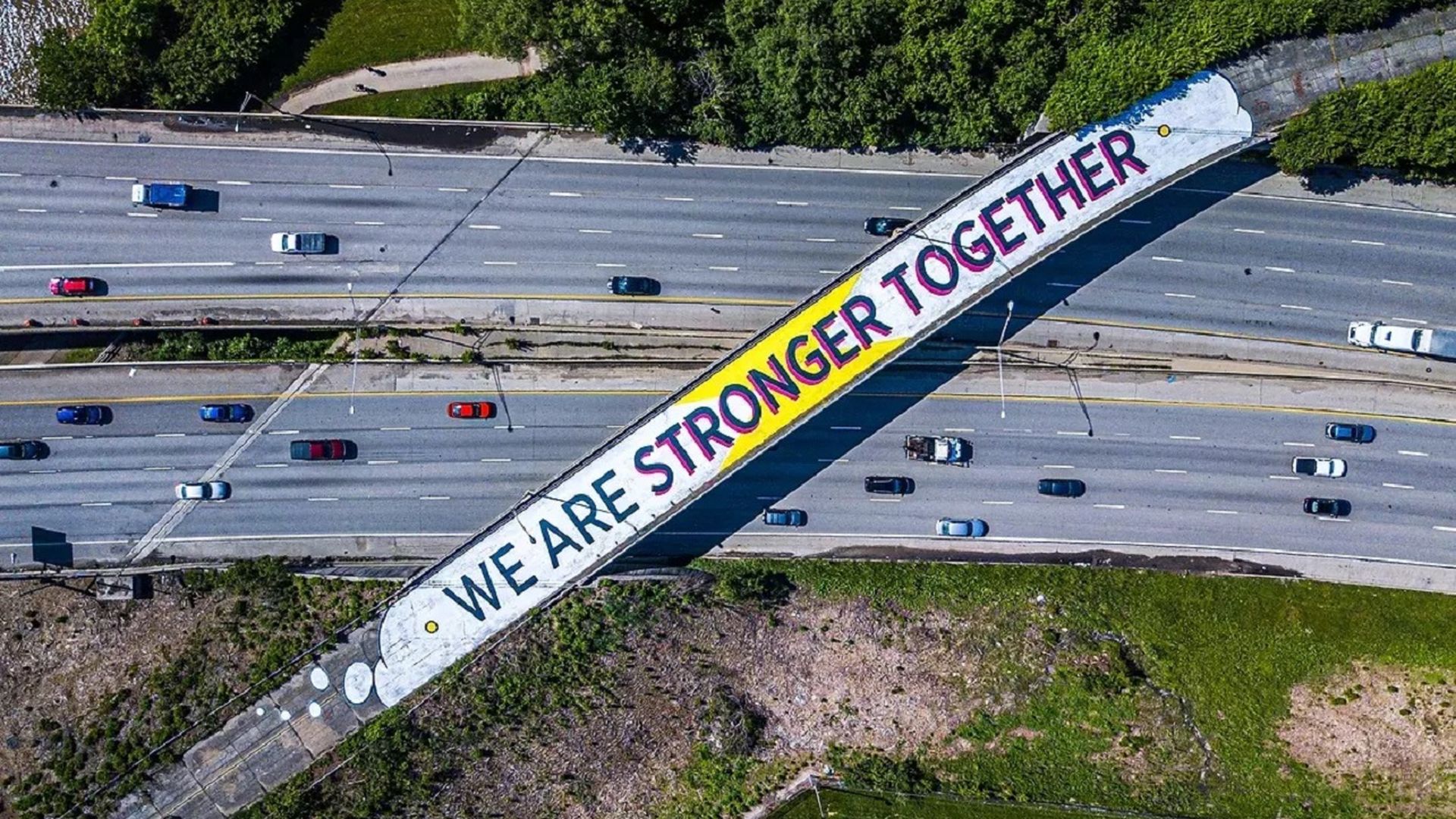 An overhead view of an abandoned highway overpass with a painted message on it reading "WE ARE STRONGER TOGETHER."