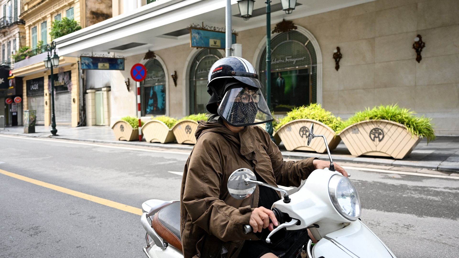 A woman wearing a face mask and shield rides her scooter along a near-empty street in Hanoi on July 24, 2021,