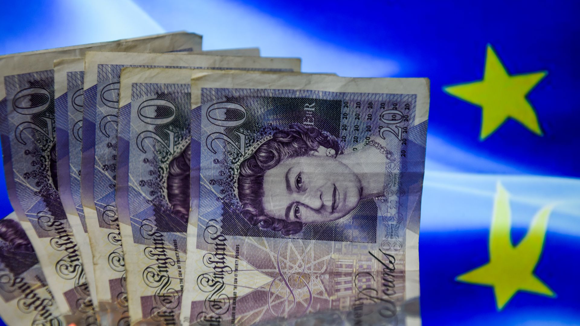 British pound notes lay on top of the EU flag. 