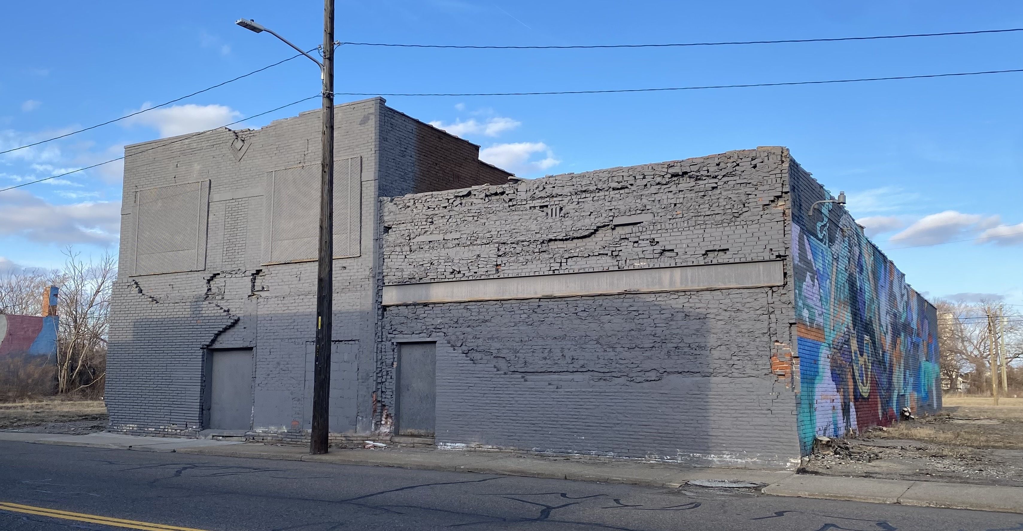 A vacant building that's grey on the front with a mural on the side.