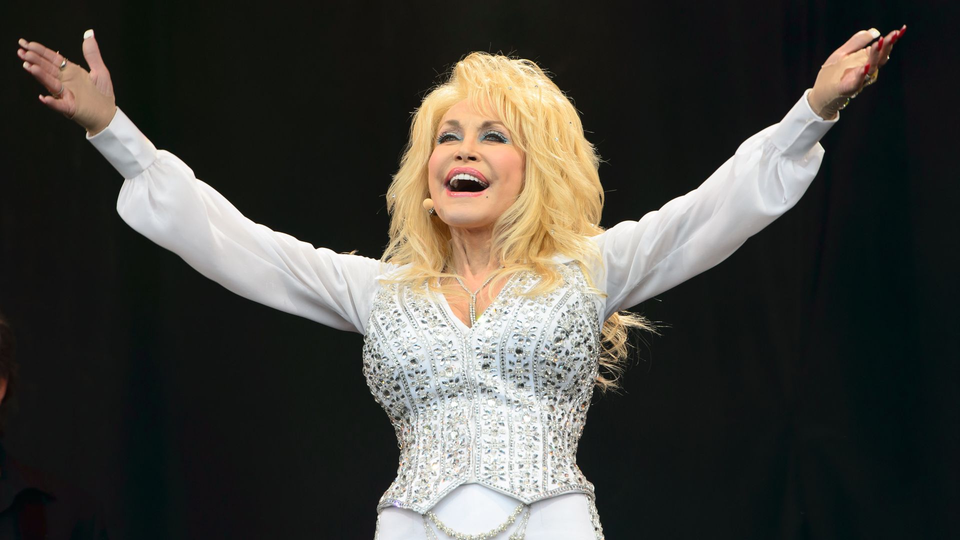Dolly Parton on stage with her arms stretched out.