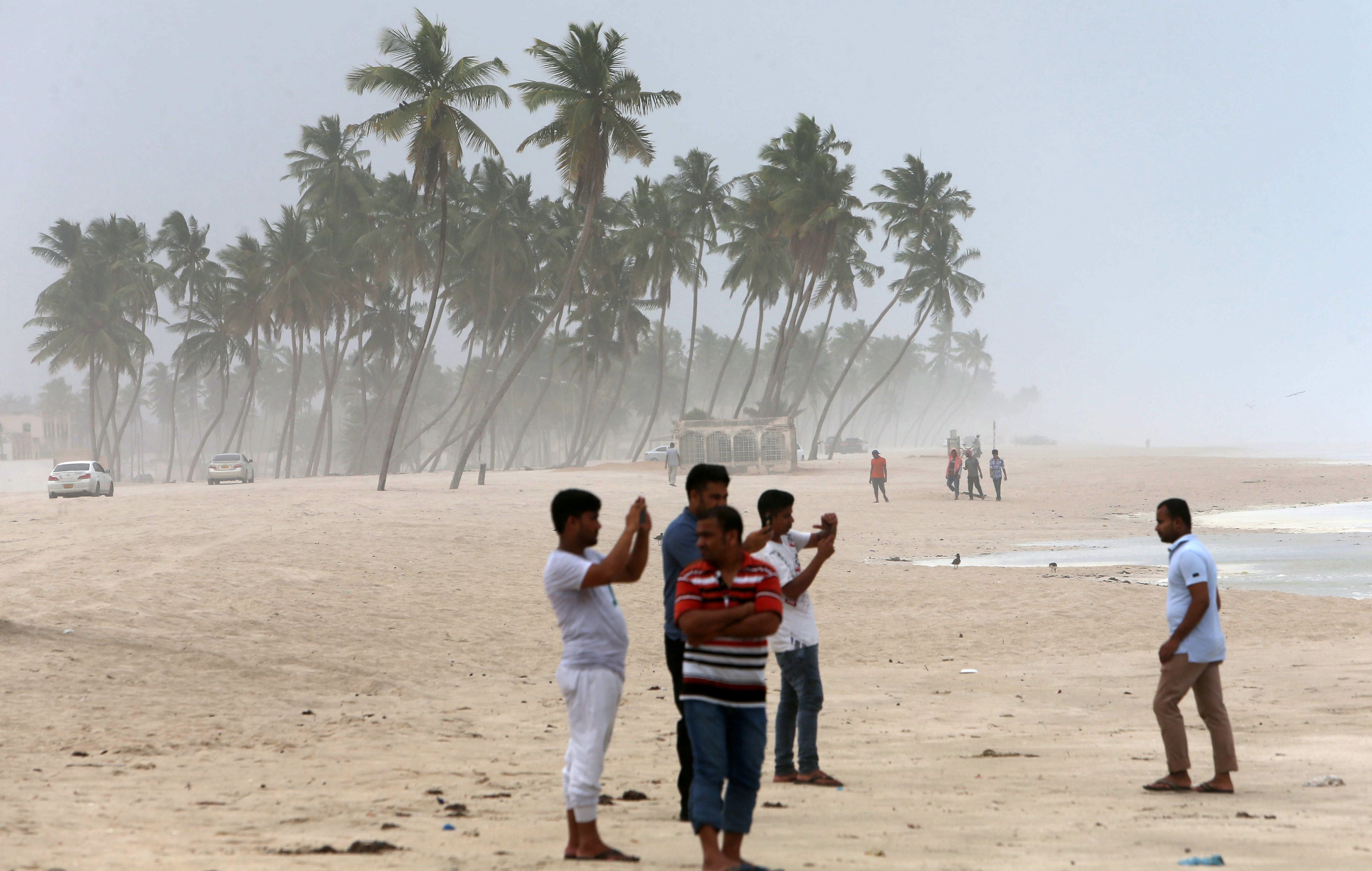 Omanis take pictures on the beach as high waves break along the shore