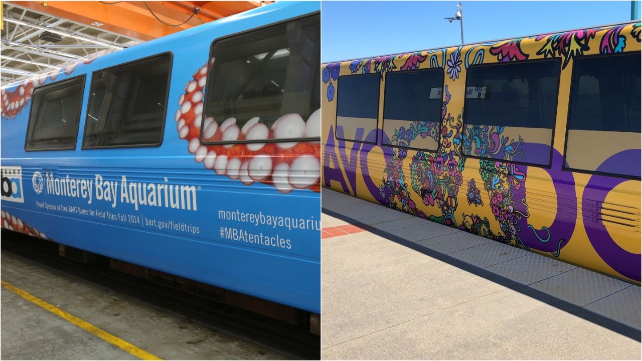 Two metro trains at a station: on the left, a bright blue train with Monterey Bay Aquarium branding and pufferfish graphics; on the right, a yellow train coated in bold purple floral graffiti.