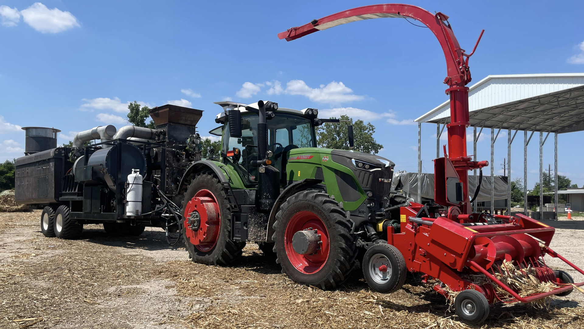 A long black Applied Carbon trailer sits hitched to a green farm tractor.