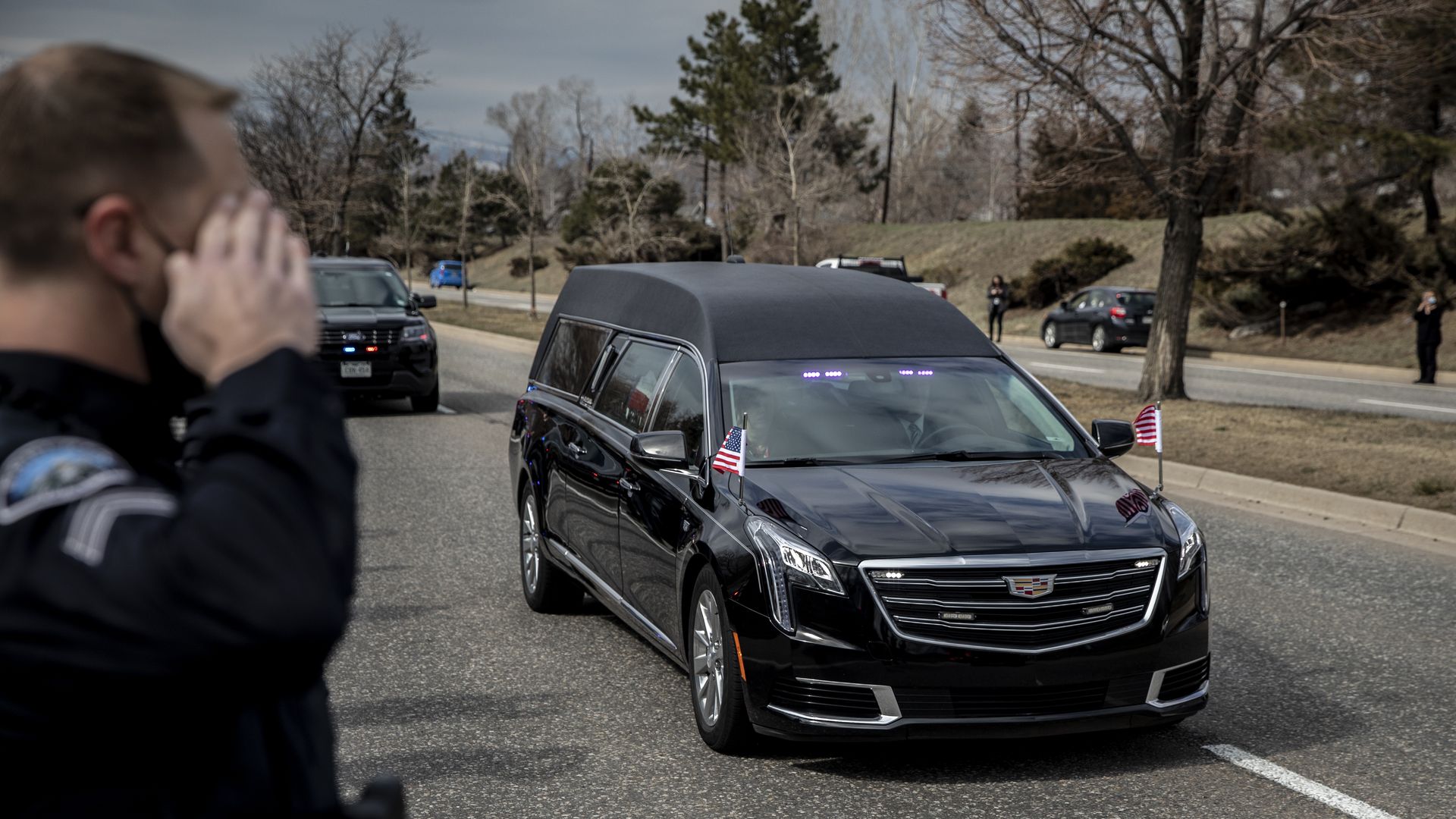 A police officer is seen saluting a hearse carrying the body of slain Boulder Police Officer Eric Talley.