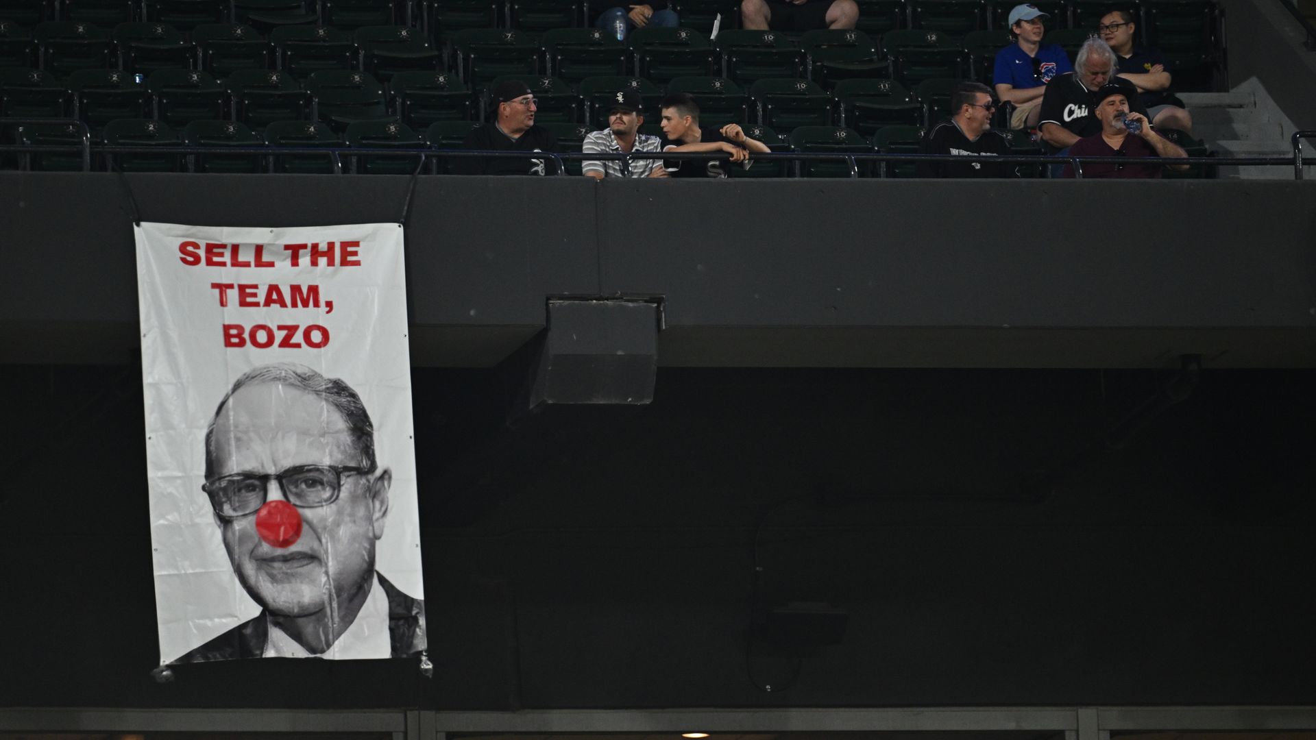 Photo of a banner that says "SELL THE TEAM, BOZO" with a man with a clown nose in the photo
