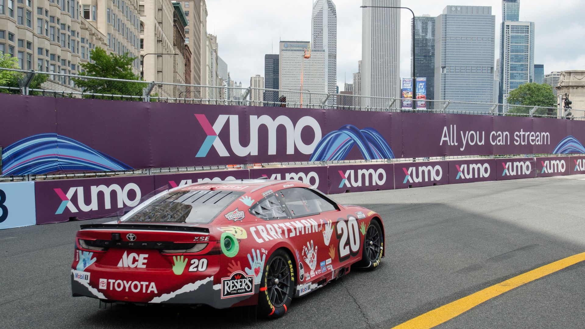 Photo of a race car driving with big buildings in background.