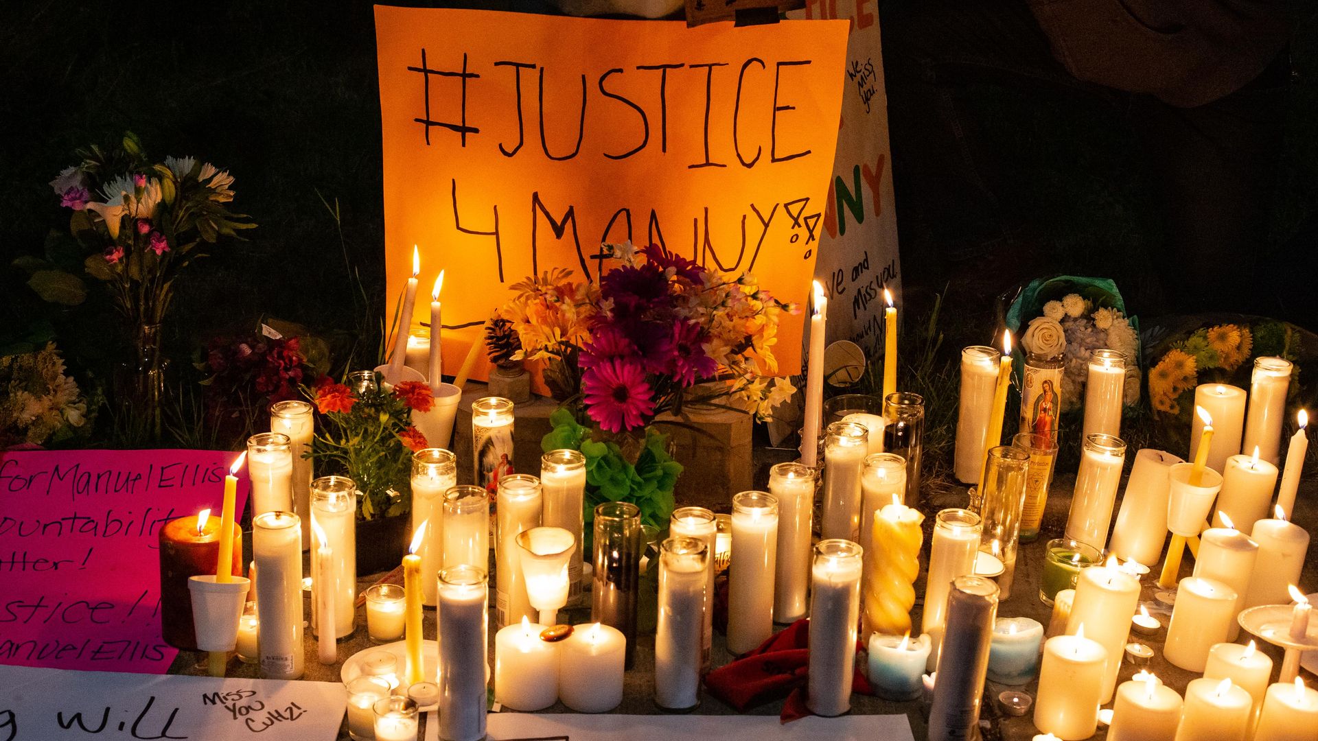 Candles surround a sign that says #Justice4Manny, with flowers.