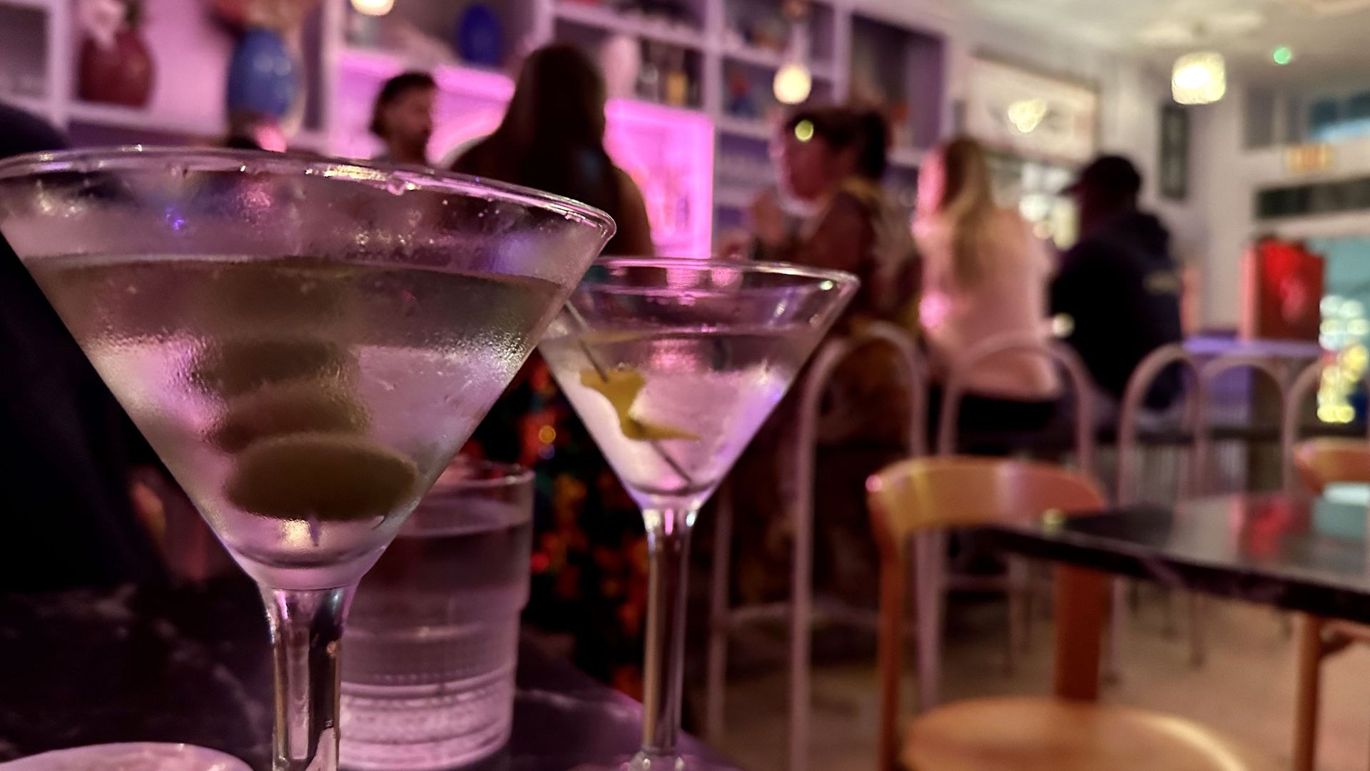 A close-up photo of two martinis with a busy bar behind them.