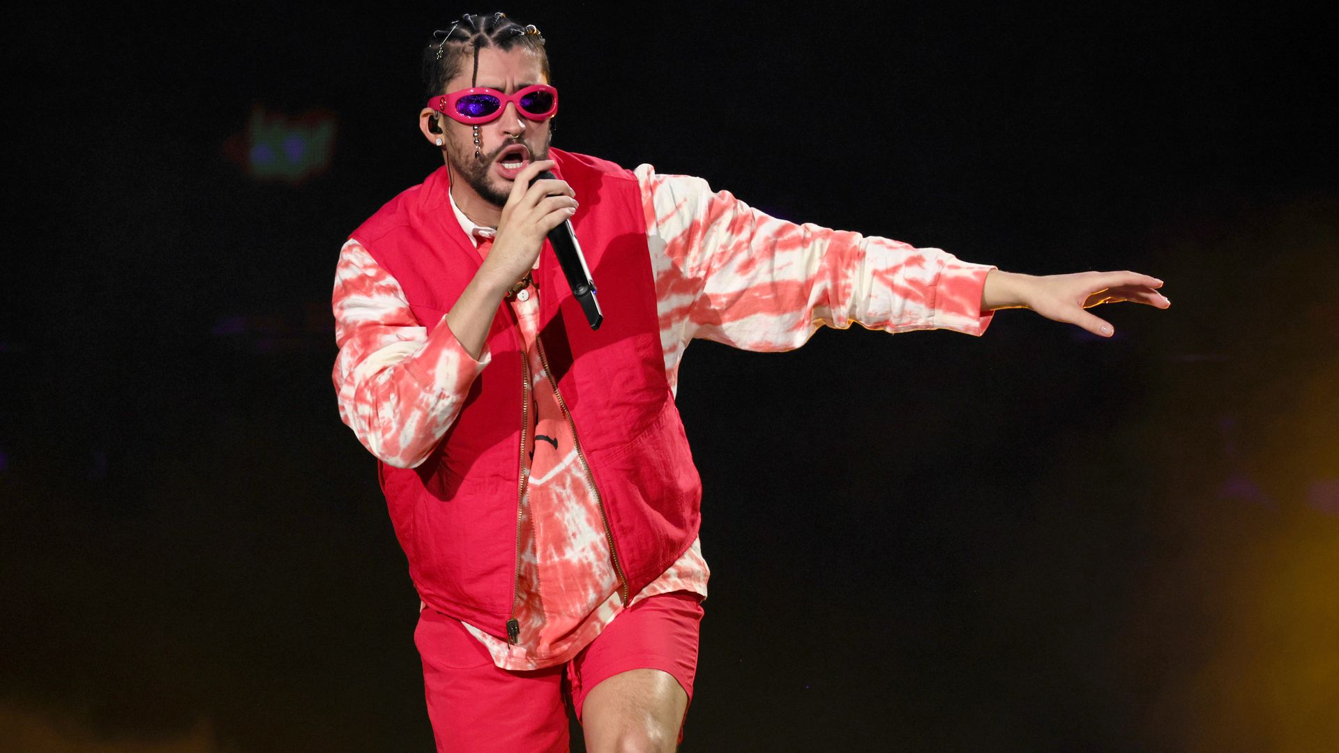 Bad Bunny wears a red outfit and red sunglasses while singing onstage 