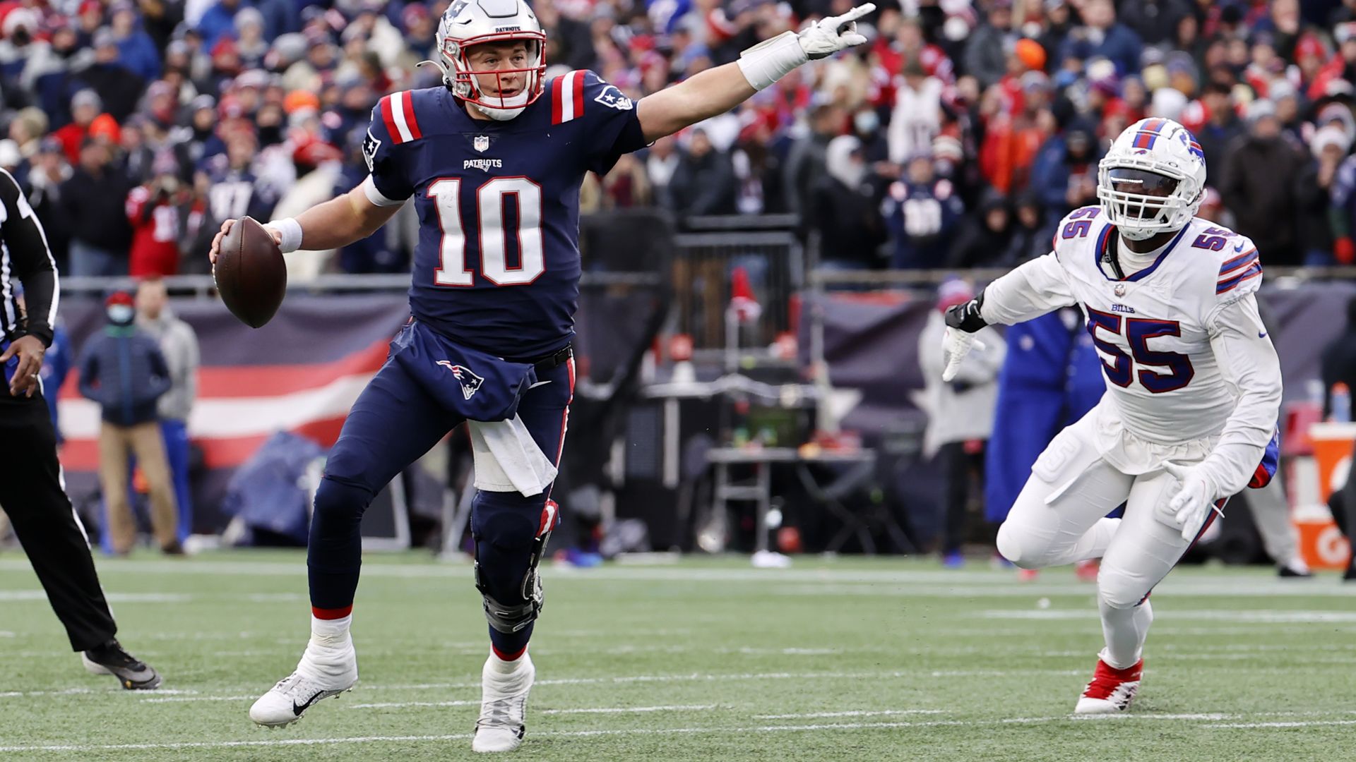 Mac Jones, the Patriots quarterback, holds a football and points as he scrambles from Buffalo Bills' defensive end.