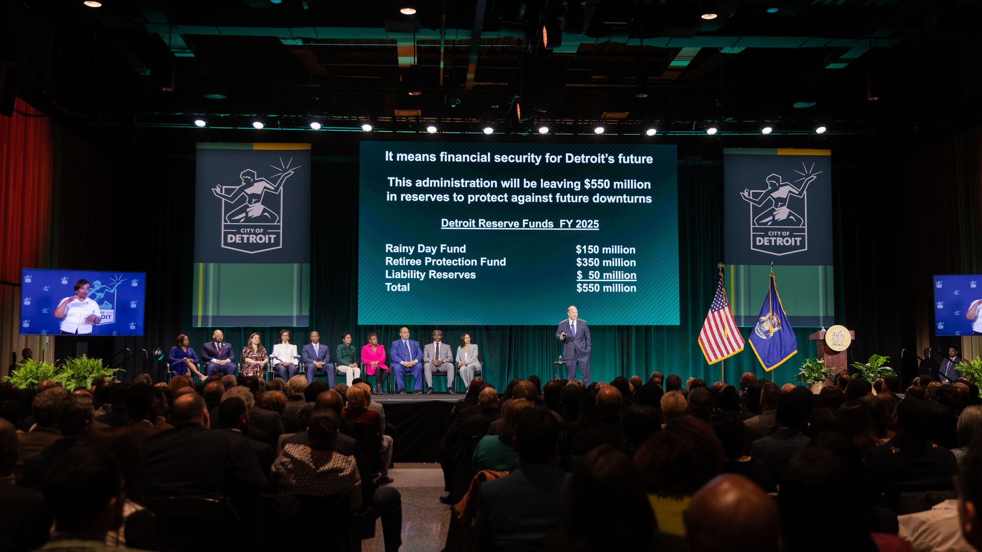 Dugan speaks in front of a crowd with a powerpoint